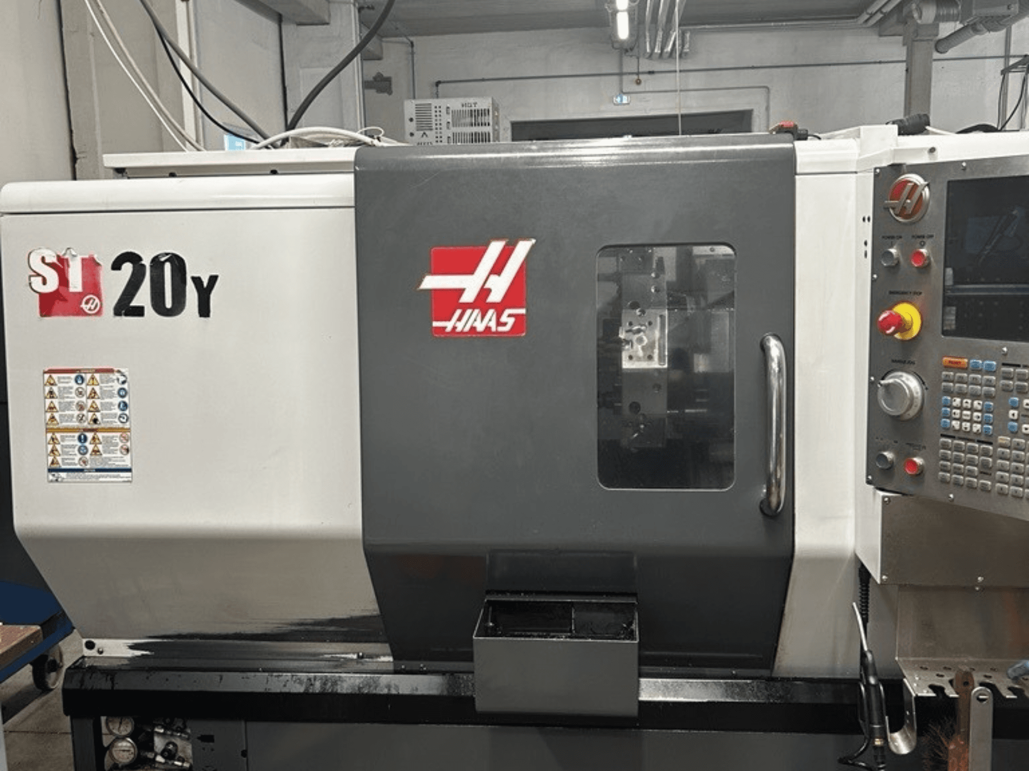 Haas ST-20Y CNC eszterga, előlnézet, a kezelőpanel, a biztonsági címkék és a kezelőablak látható.