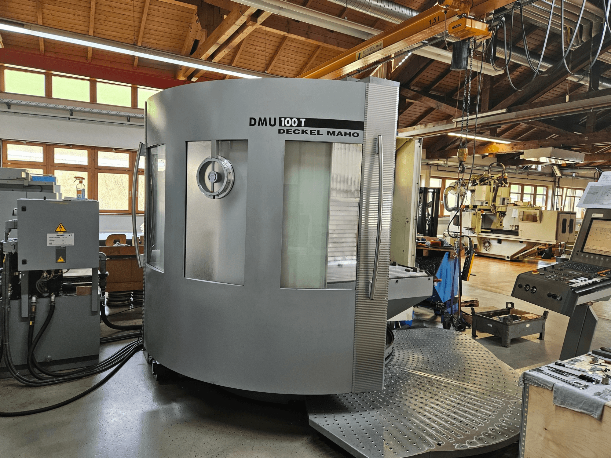DMU 100 T Deckel Maho CNC gép szemből nézve, nagy kör alakú talapzattal, vezérlőpanellel és üvegburkolattal.