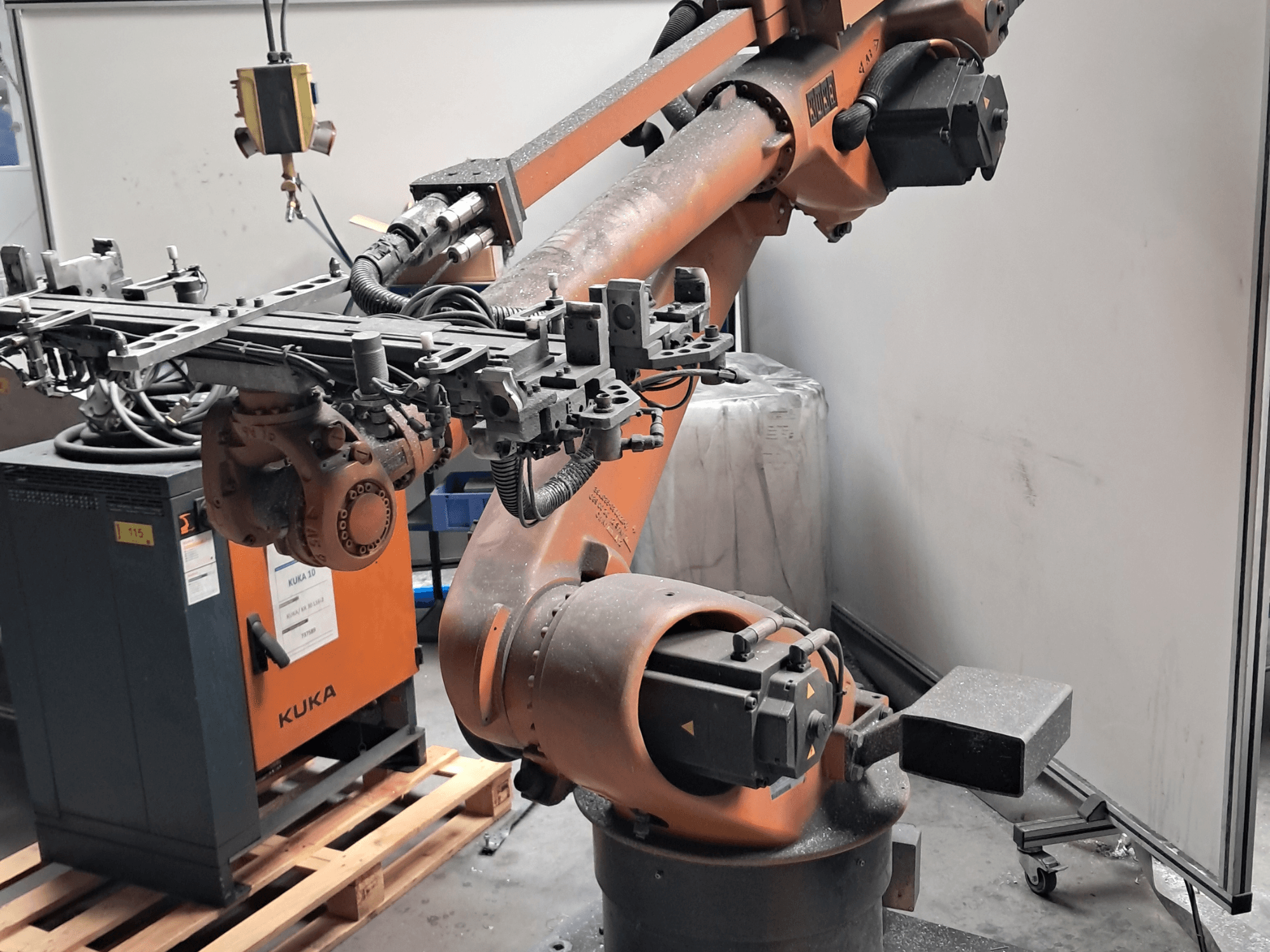 A KUKA KR 30L16-2 robotkar oldalnézetben, bonyolult végberendezéssel és vezérlőkábelekkel, egy KUKA vezérlődoboz mellett.