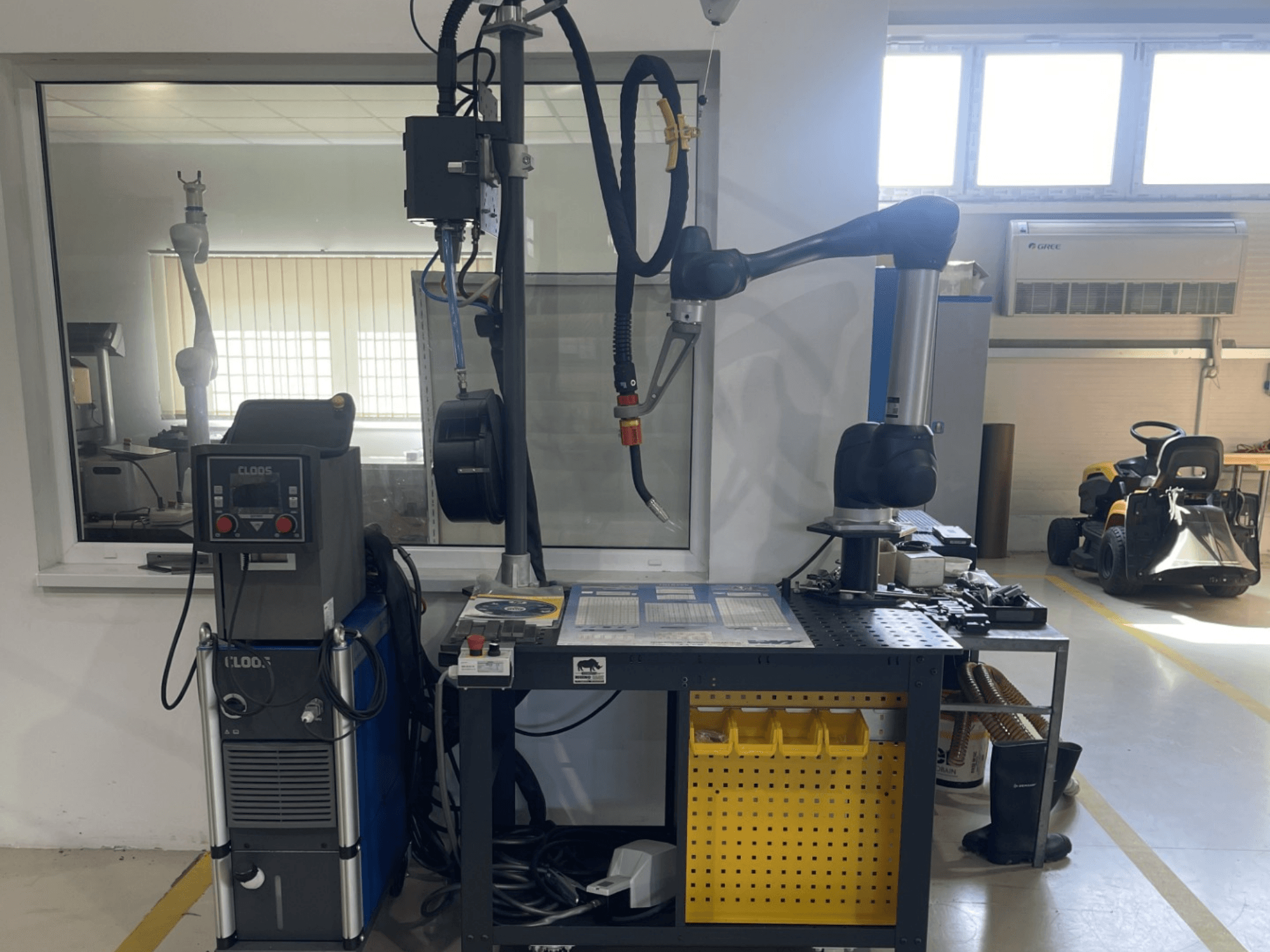 DOOSAN M1013 együttműködő robot egy műhelyben, oldalnézetben, hegesztőberendezéssel és szerszámokkal a munkapadon.