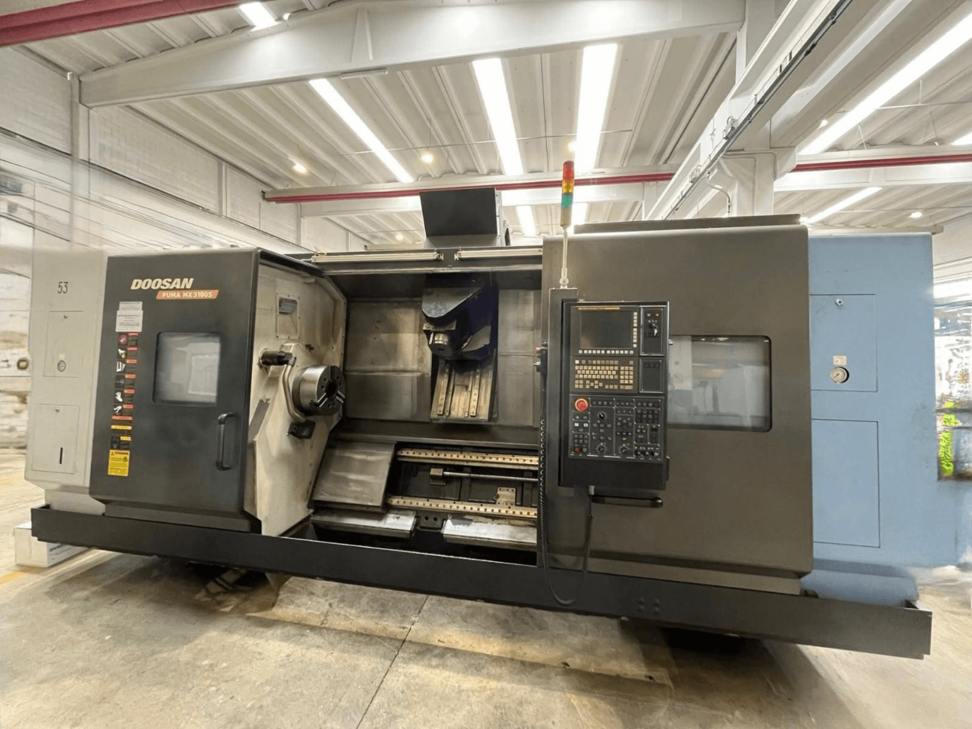 A DOOSAN PUMA MX3100 vízszintes eszterga elölnézete, a vezérlőpanellel, valamint a látható orsóval és szerszámtartóval.
