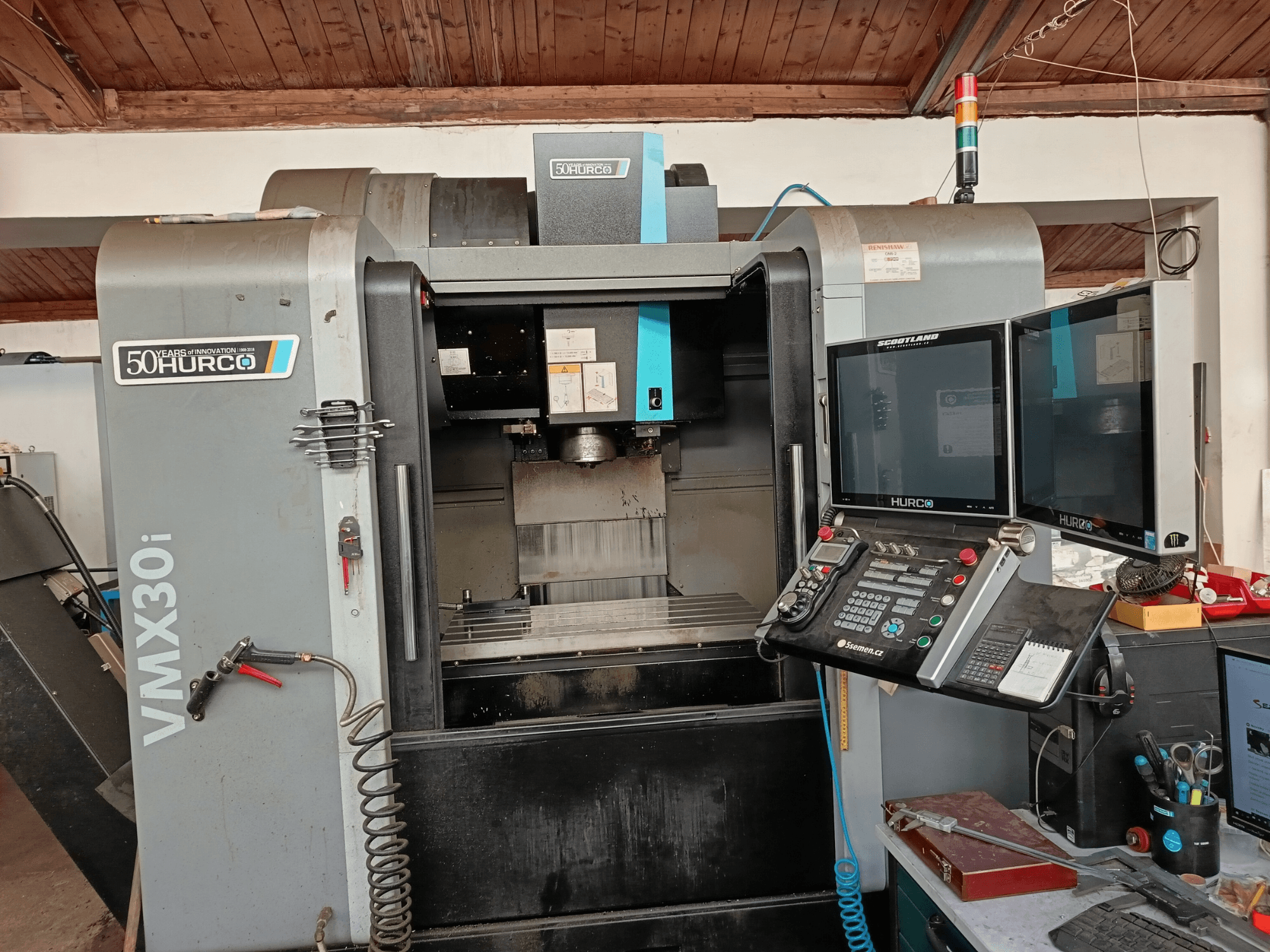 Hurco VMX30i CNC marógép elölnézetben, két monitorral, vezérlőpanellel és egy csatlakoztatott tömlővel.