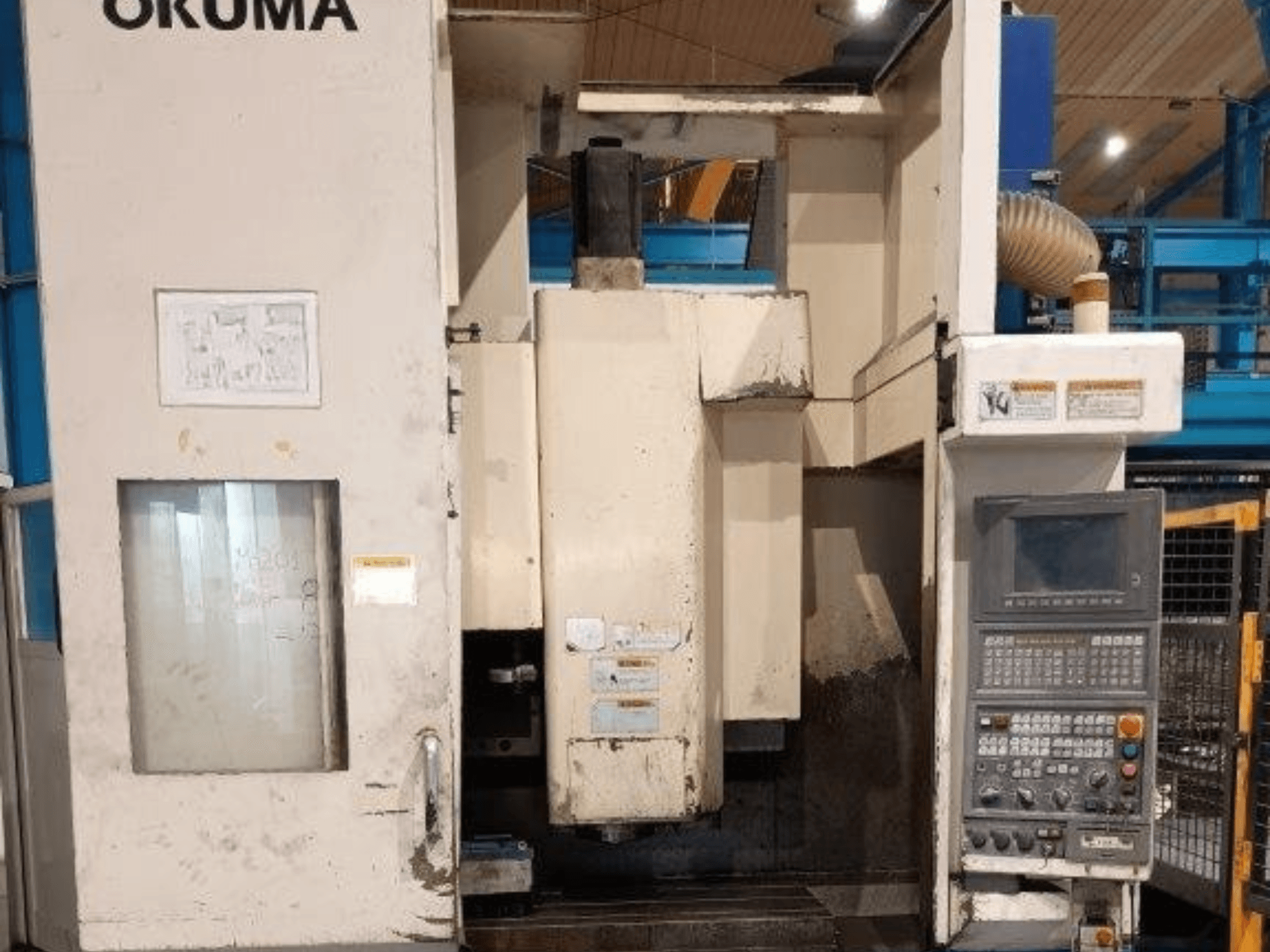 Okuma CNC marógép, elölnézet, a géptestben látható gombokkal ellátott kezelőpanel, kijelző és látható jelek.