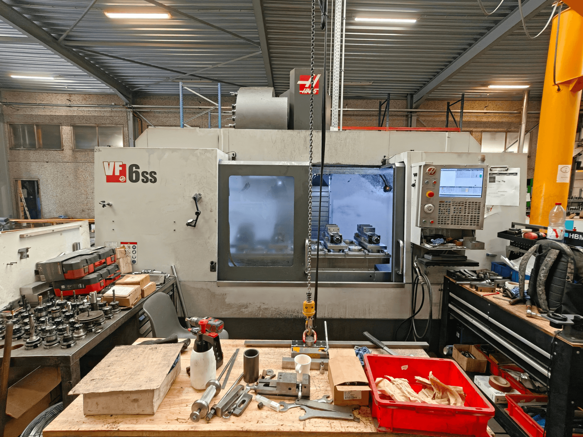 Haas VF-6SS függőleges megmunkáló központ egy műhelyben, oldalnézetből, amelyen látható a vezérlőpanel és a szerszámokkal teli munkaterület.
