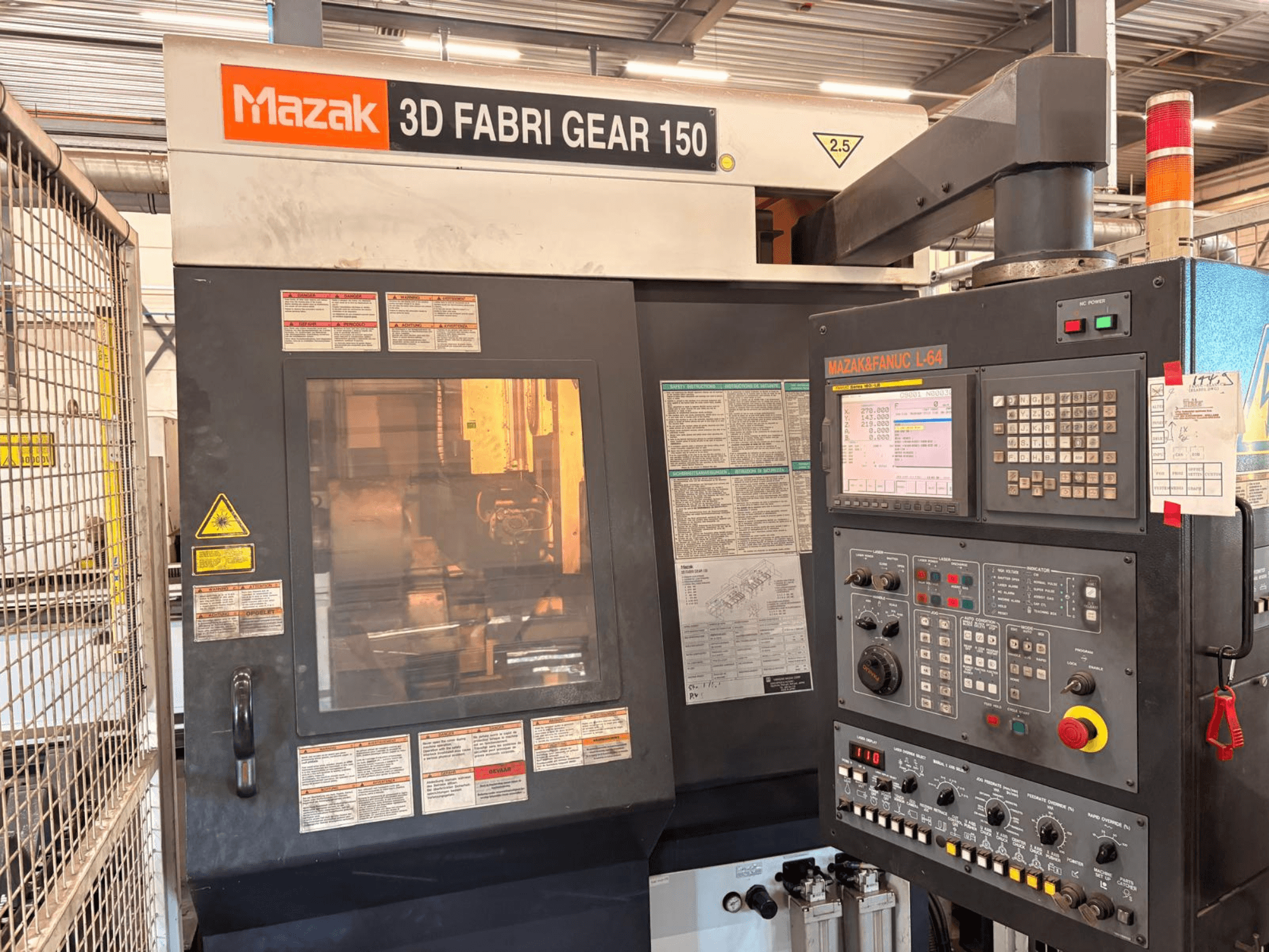 Mazak 3D Fabri Gear 150 csővágó gép, elölnézet, amelyen látható a vezérlőpanel, a biztonsági címkék és a kezelőfelület.