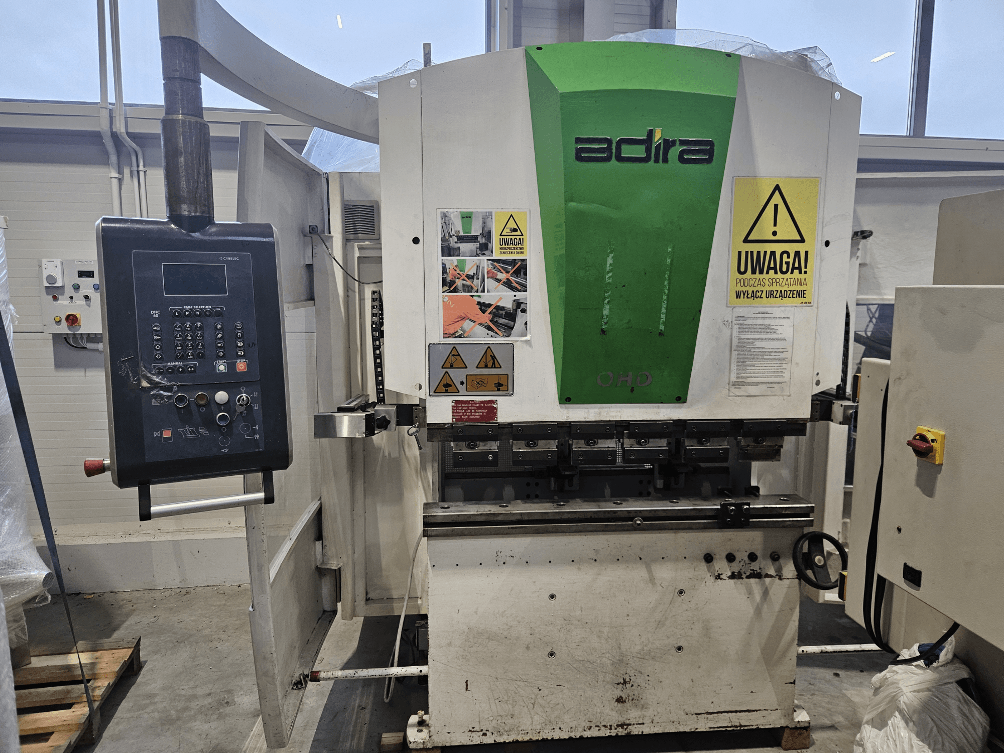 Adira OHD gép elölről nézve, a kezelőpanellel, a biztonsági figyelmeztetésekkel és a kezelőgombokkal.