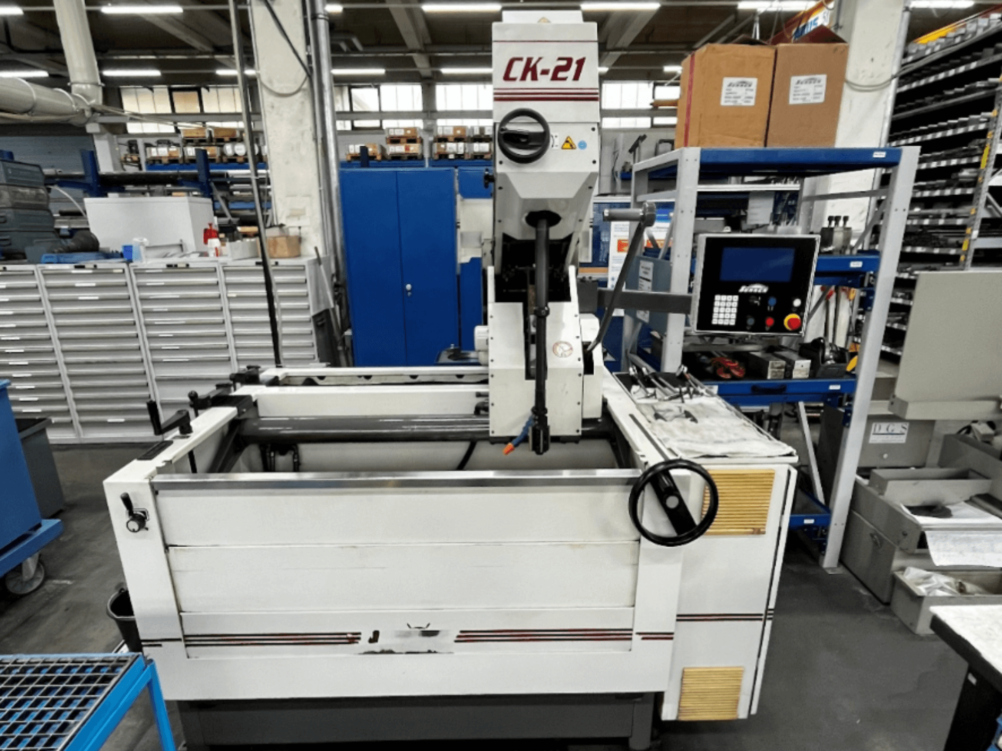 A Sunnen CK-21-CC függőleges csiszológép elölnézetben, háttérben a vezérlők, a csiszolási terület és a segédberendezések.