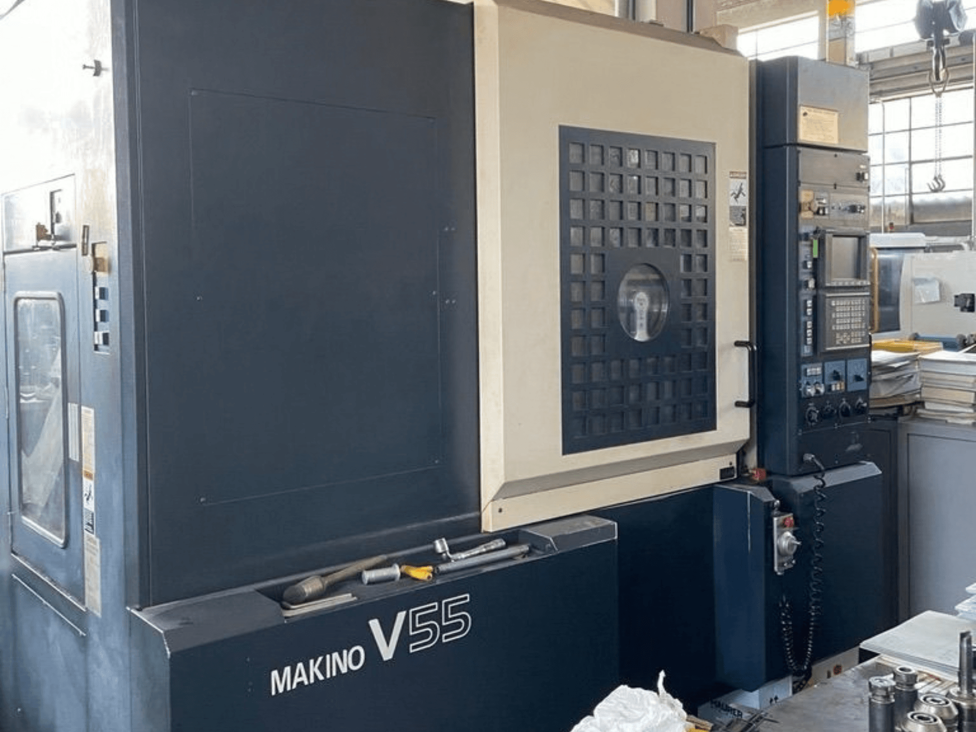 Makino V55-A15 függőleges megmunkáló központ, elölnézet a vezérlőpanellel, a masszív felépítéssel és a munkaterület elrendezésével.
