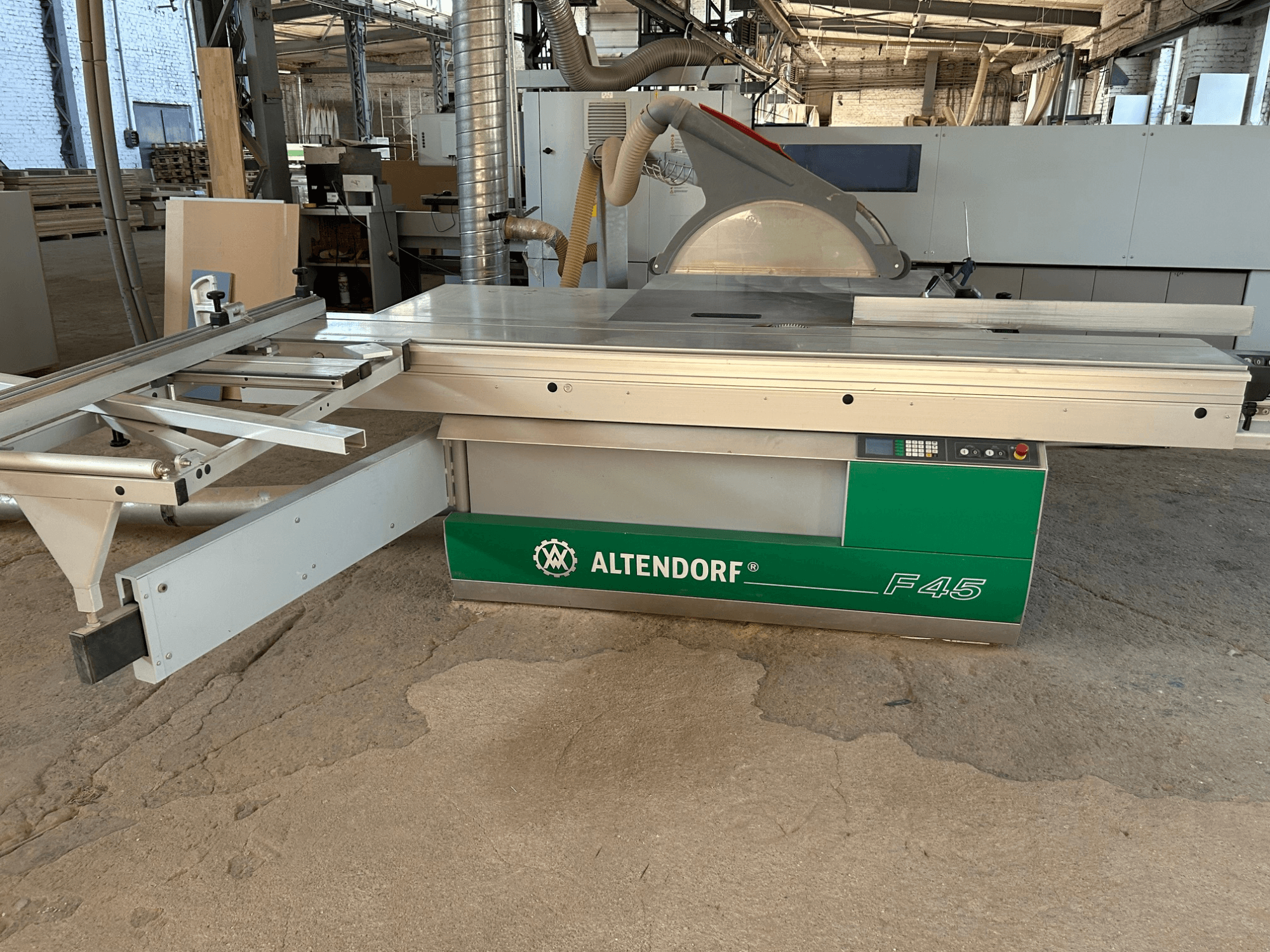 Altendorf F 45 lemezfűrész, elölnézet, amelyen látható a vágóasztal, a fűrészlapvédő és a kezelőpanel a zöld és szürke gépen.