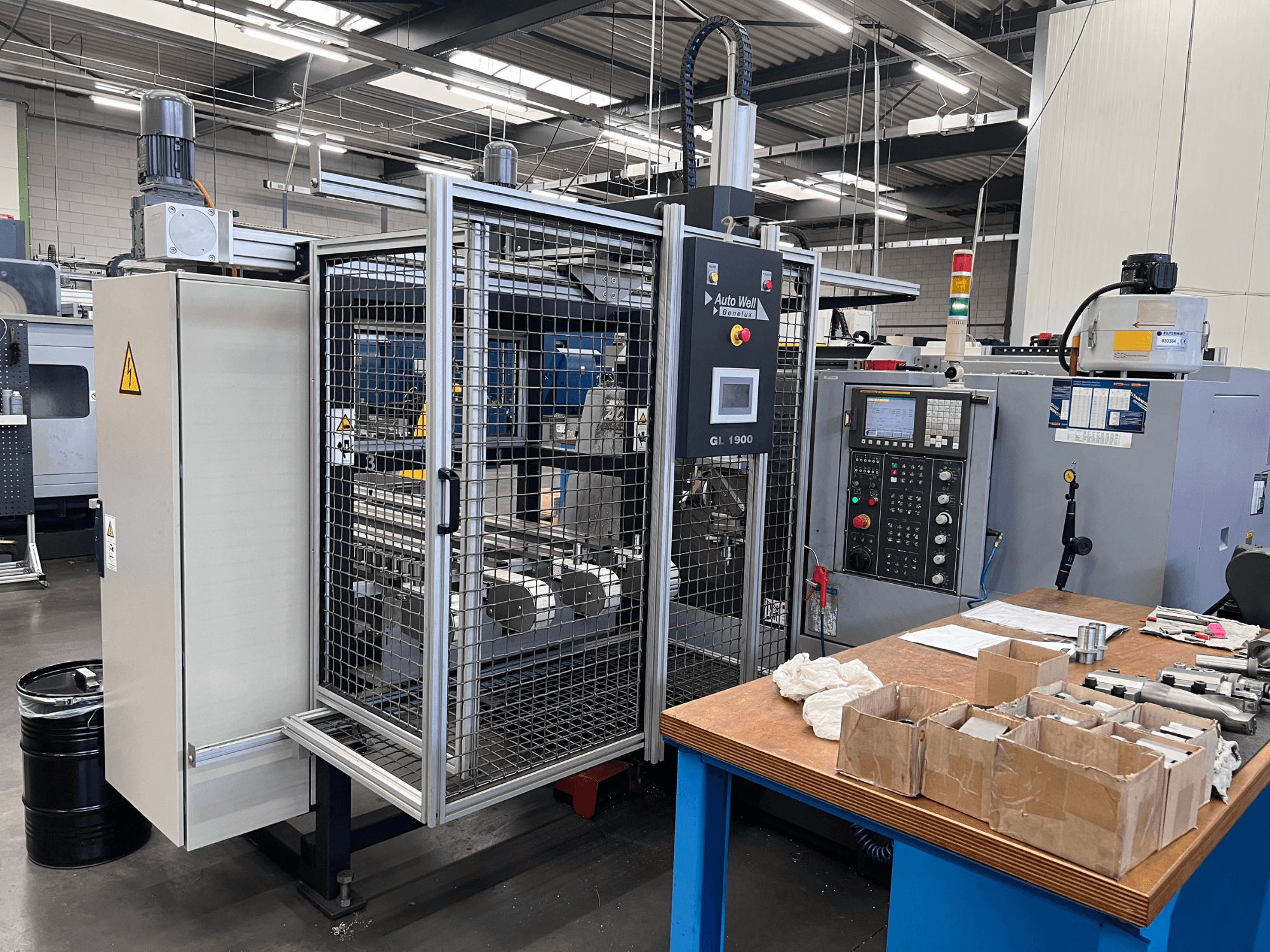 Az Auto Weld GL 1900 gép előlapja a vezérlőpanellel, a biztonsági burkolattal és a környező szerszámokkal egy munkapadon.