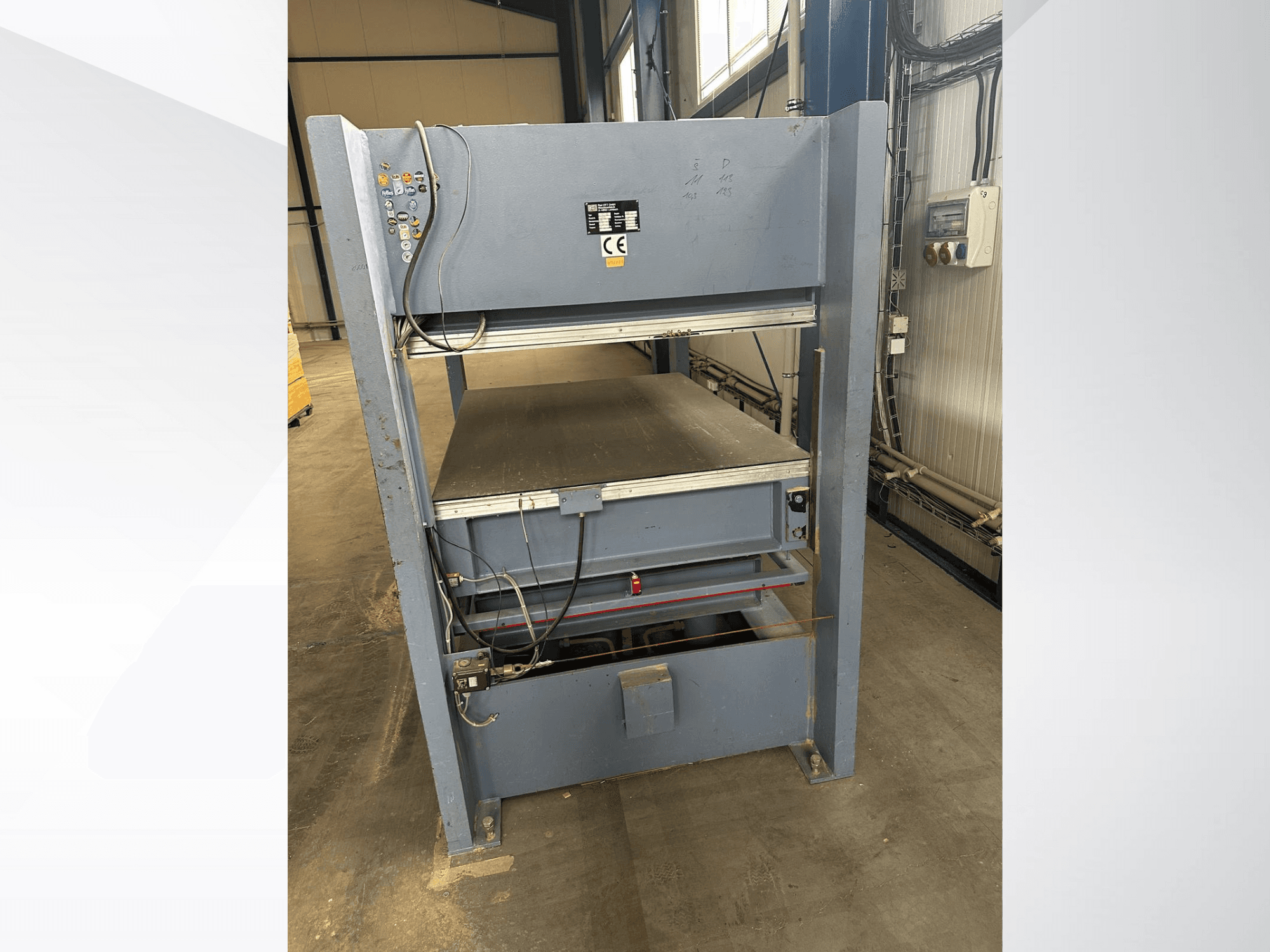 Szürke ipari gép szemből nézve, vezérlőpanellel; állítható platformokkal és biztonsági jelölésekkel.