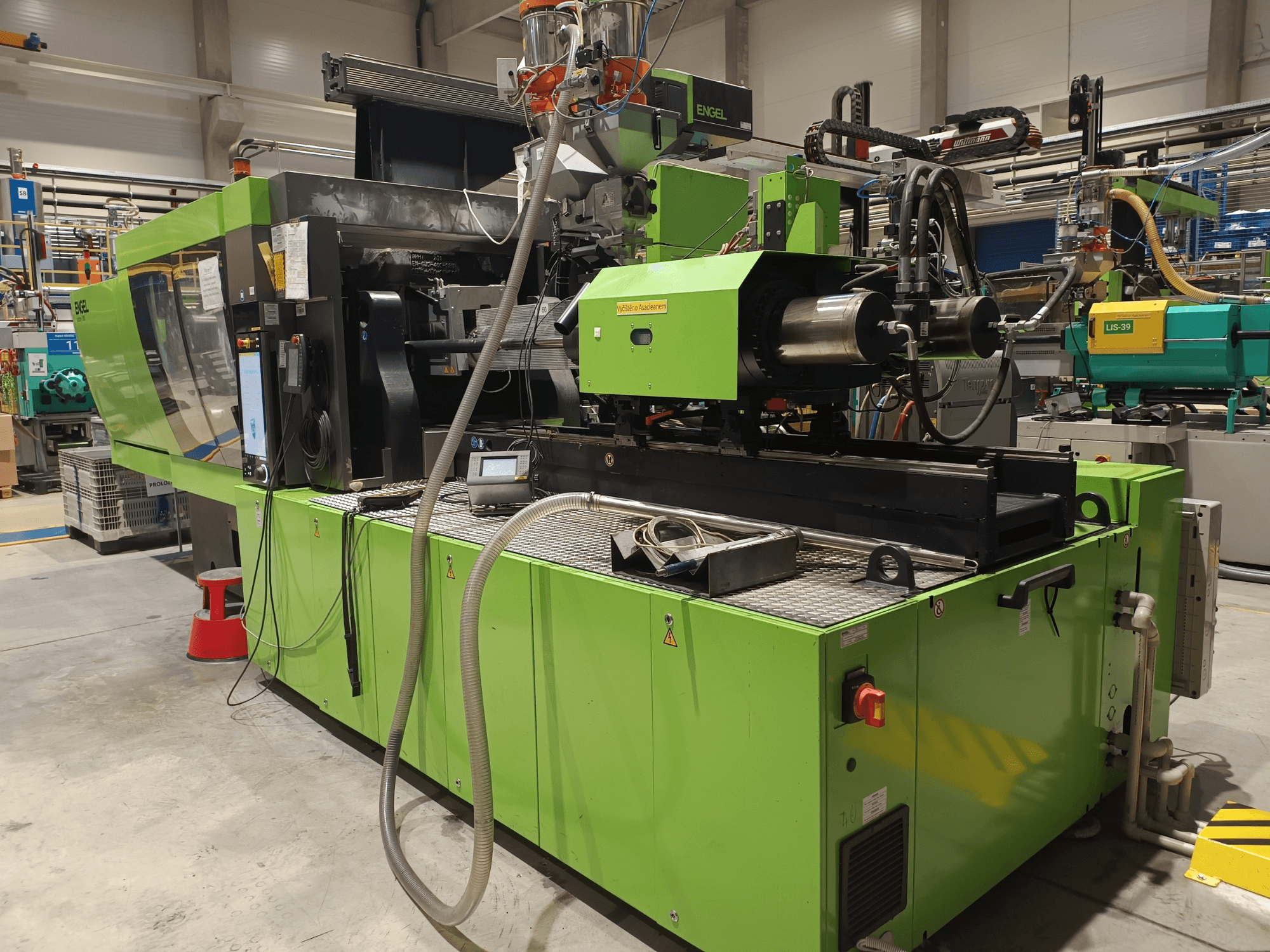 Engel fröccsöntőgép, oldalnézet, zöld külső, látható az érintőképernyős panel és a hidraulikus alkatrészek.