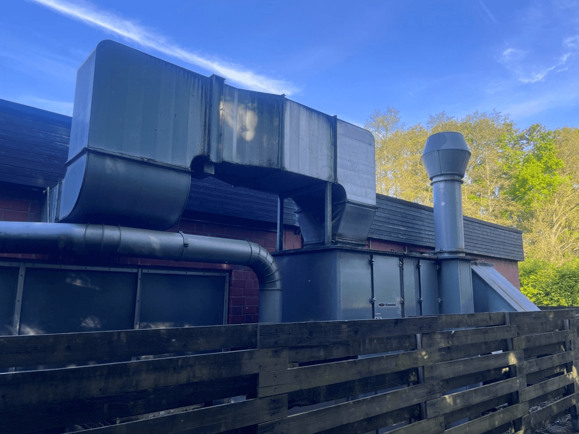 Ipari szellőzőrendszer fémcsatornákkal, oldalnézet; négyzet alakú és hengeres kéményt tartalmaz, zöld kivitelben.