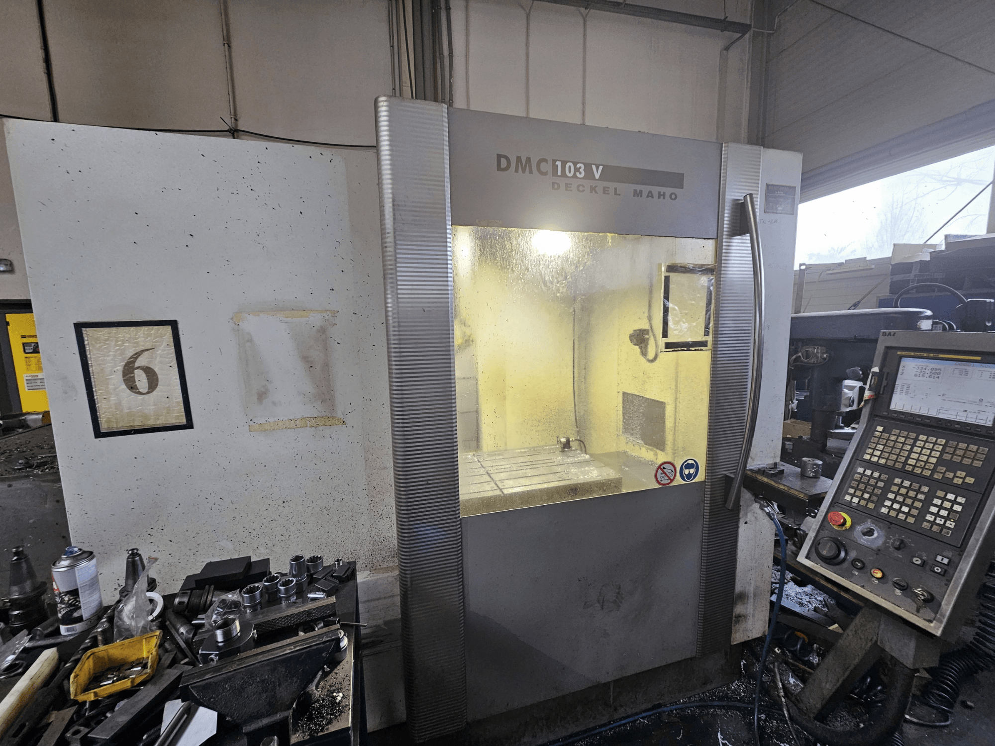 Egy Deckel Maho DMC 103 V CNC-gép elülső nézete, a vezérlőpanel, a munkaterület és a "6" számozott jelző.
