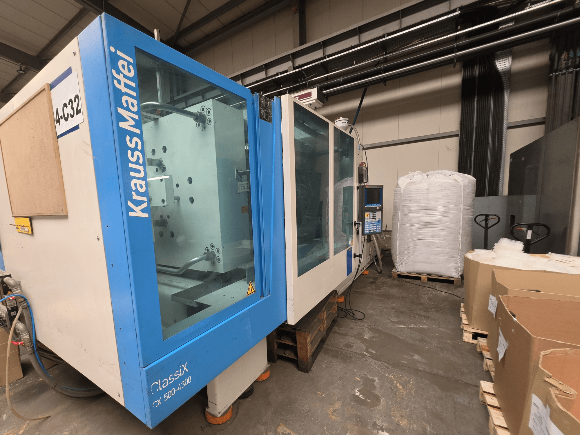 Krauss Maffei 500-4000 CX hidraulikus fröccsöntőgép, oldalnézet, a vezérlőpanel és a közeli csomagolóanyagok bemutatása.