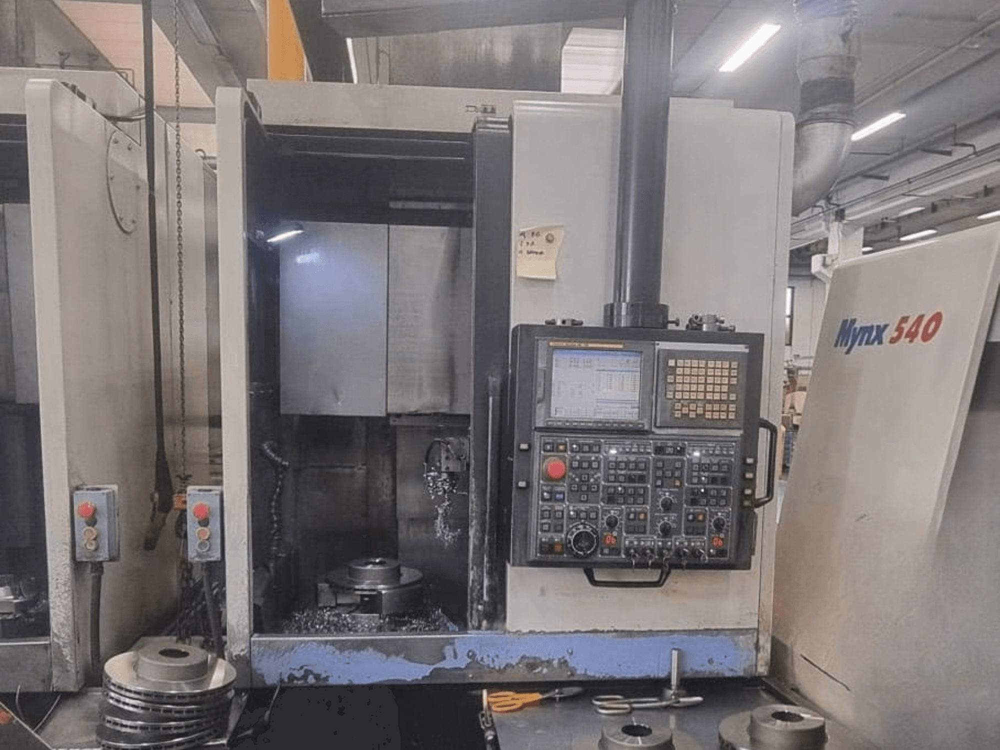 A DOOSAN PUMA V400-2SP függőleges eszterga elölnézete, amelyen látható a vezérlőpanel és a gép belsejében elhelyezett munkadarab.