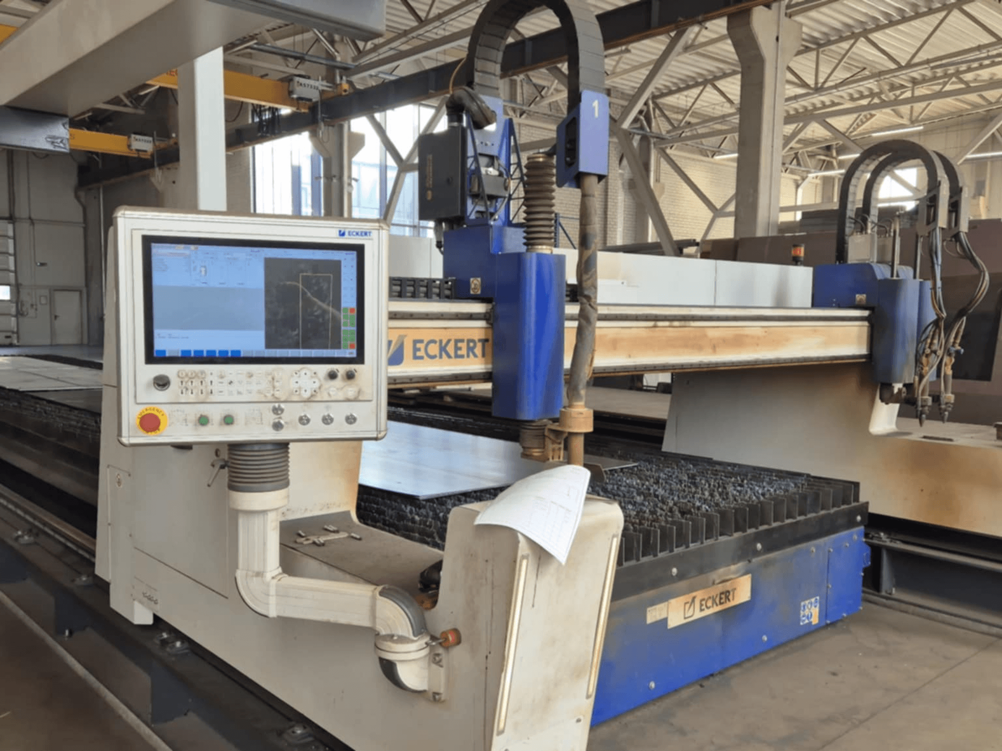 Az ECKERT CNC-vágógép vezérlőpanelje elölnézetben, érintőképernyős kijelzővel és különböző kezelőgombokkal.