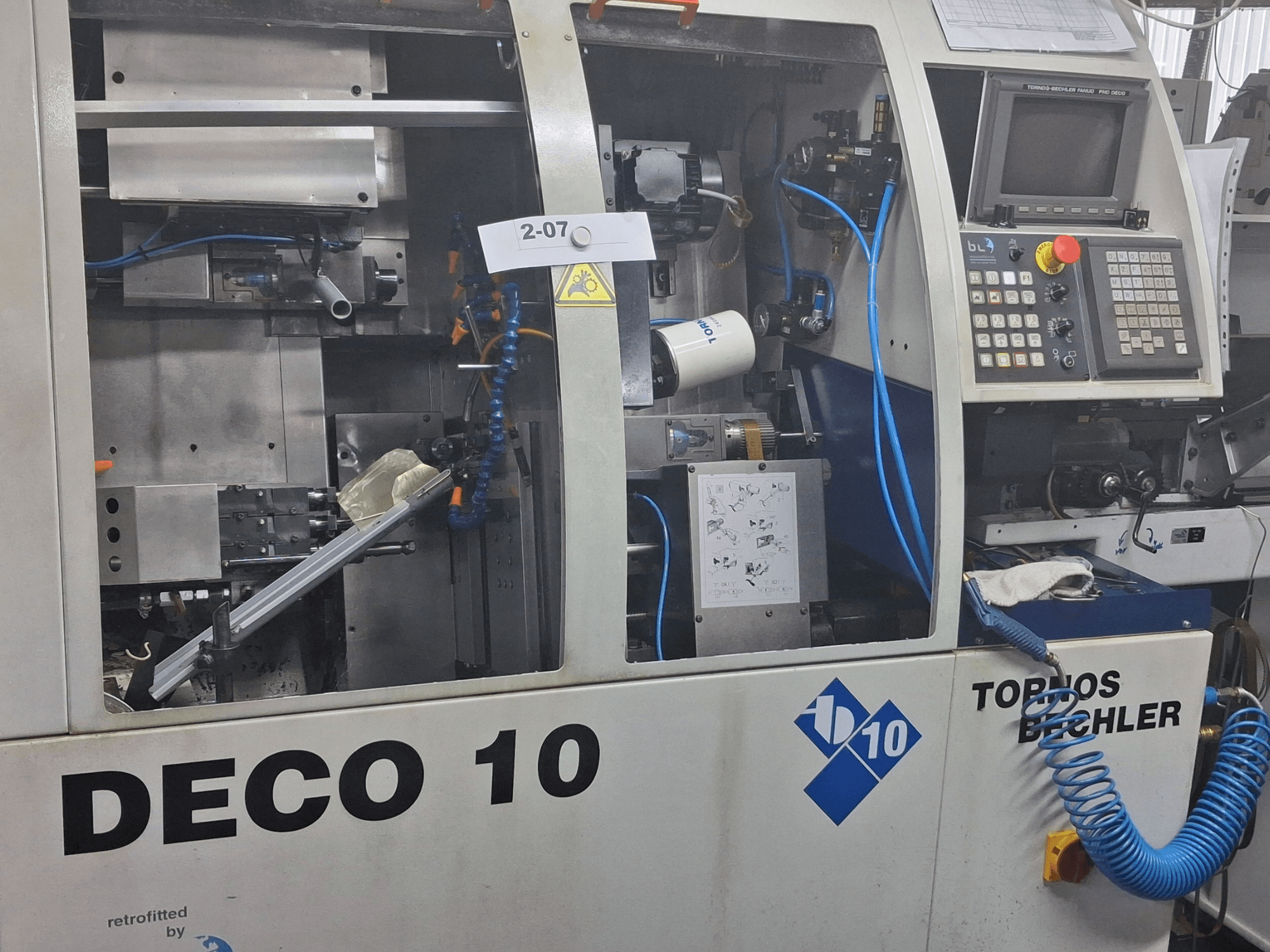 Közelkép a TORNOS Deco 10a svájci típusú esztergagépről, a belső mechanizmus és a vezérlőpanel részleteinek bemutatásával.