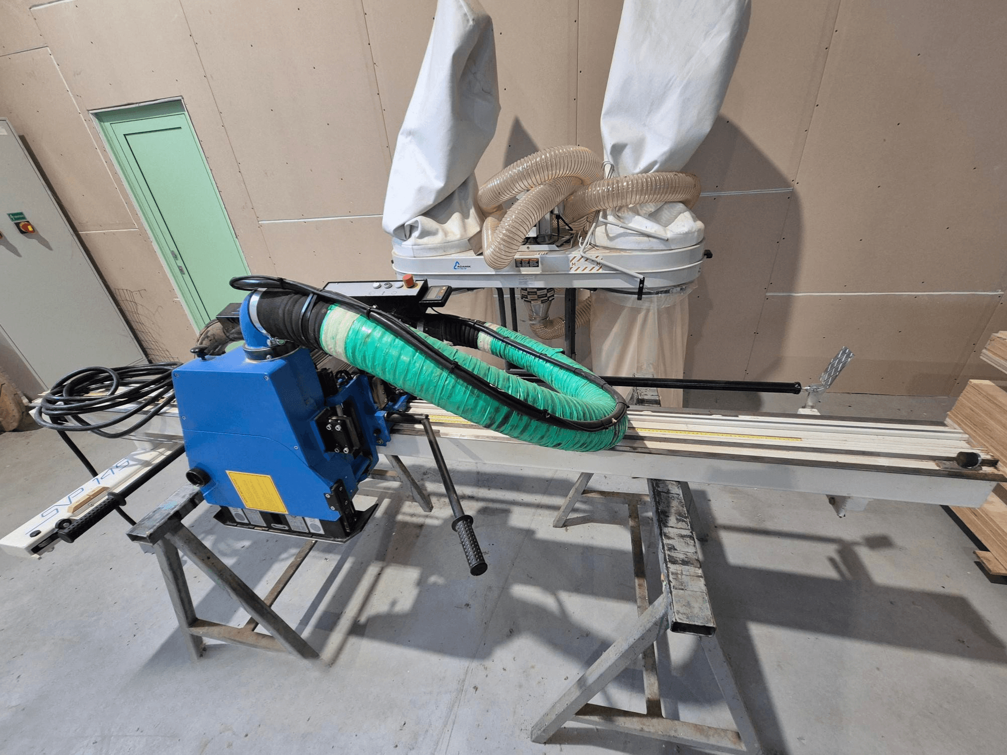Kék SVP-175 vízszintes lemezfűrész zöld porzsákkal és tartóval, oldalnézetből, műhelyben.