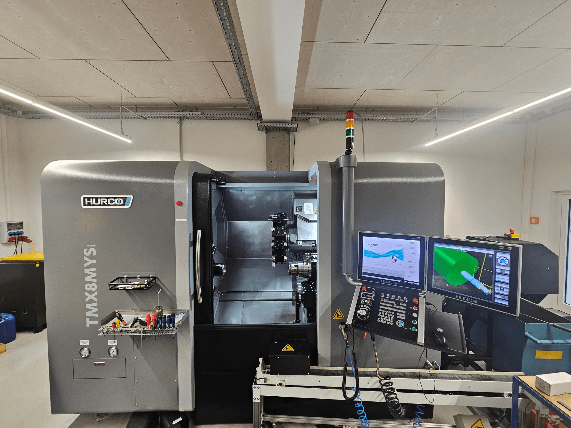 Hurco TMX 8 MYSi esztergapadozó központ egy műhelyben, kettős monitorral, vezérlőpanellel és szerszámokkal az oldalán.