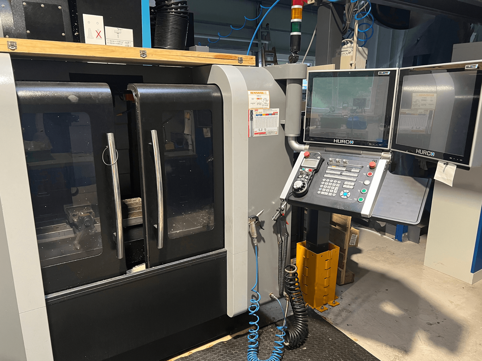 Hurco CNC gép előlapja kettős monitorral és vezérlőpanellel. Átlátszó ajtókkal és belülről látható megmunkálási területtel rendelkezik.