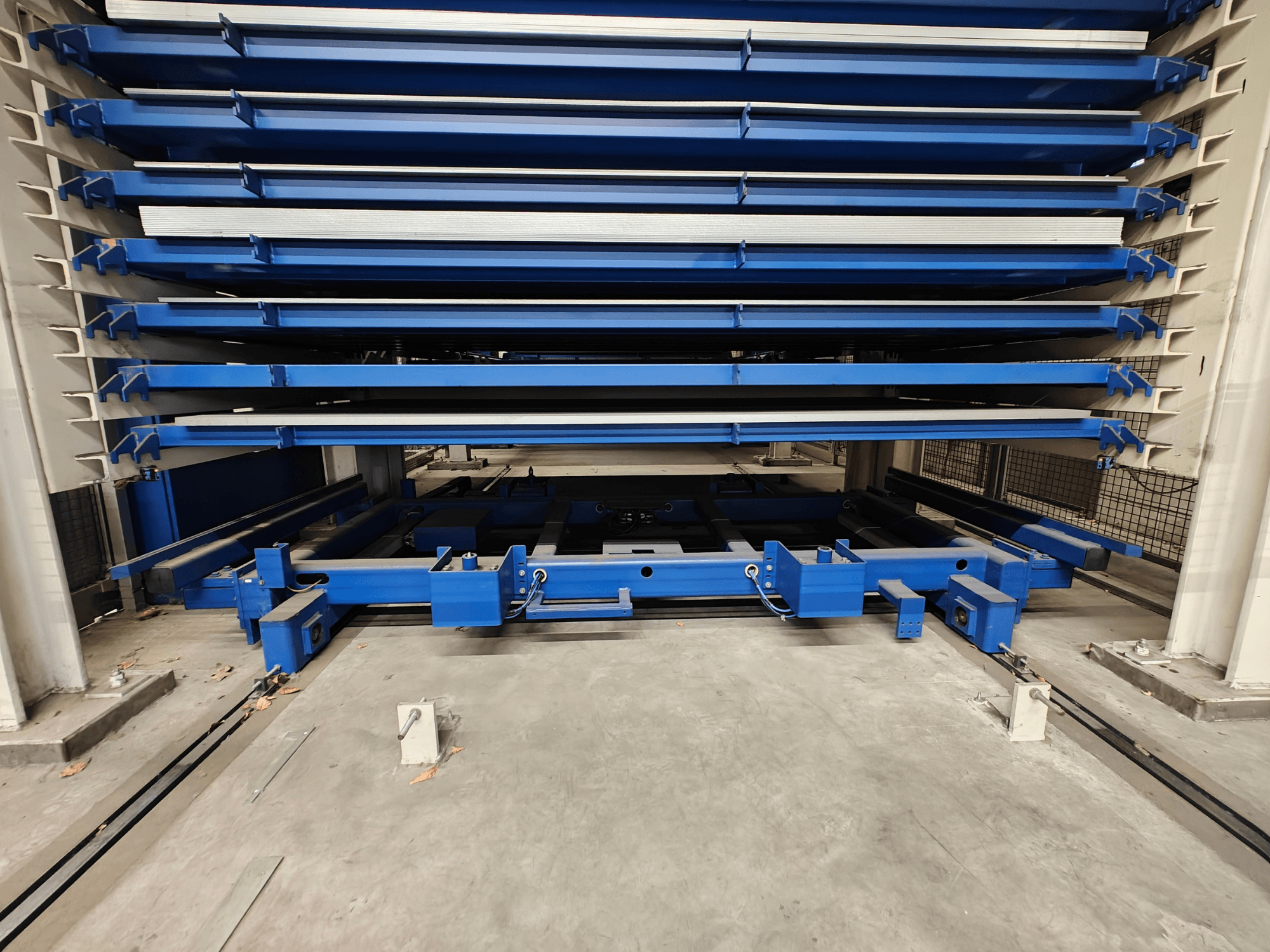 Kék ipari tárolóállvány több vízszintes polccal, szemből nézve. Emelőmechanizmussal és tartógerendákkal rendelkezik.