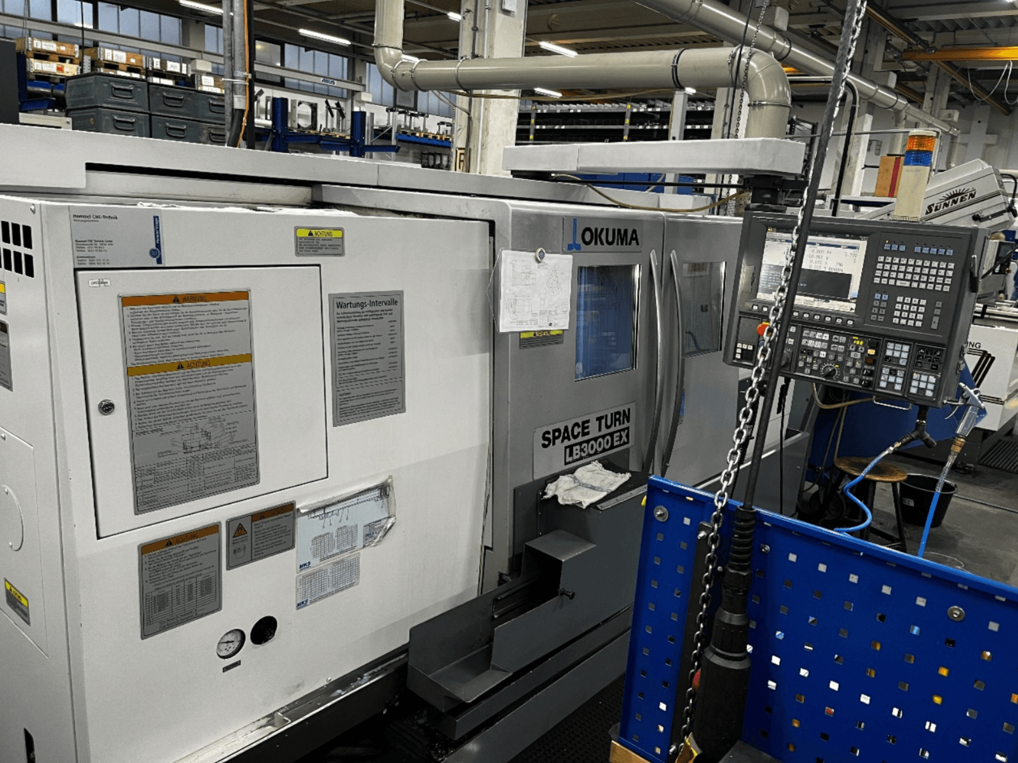 Okuma LB3000 EX vízszintes esztergagép, elölnézet, az oldalán a kezelőpanel és a biztonsági információk megjelenítése.