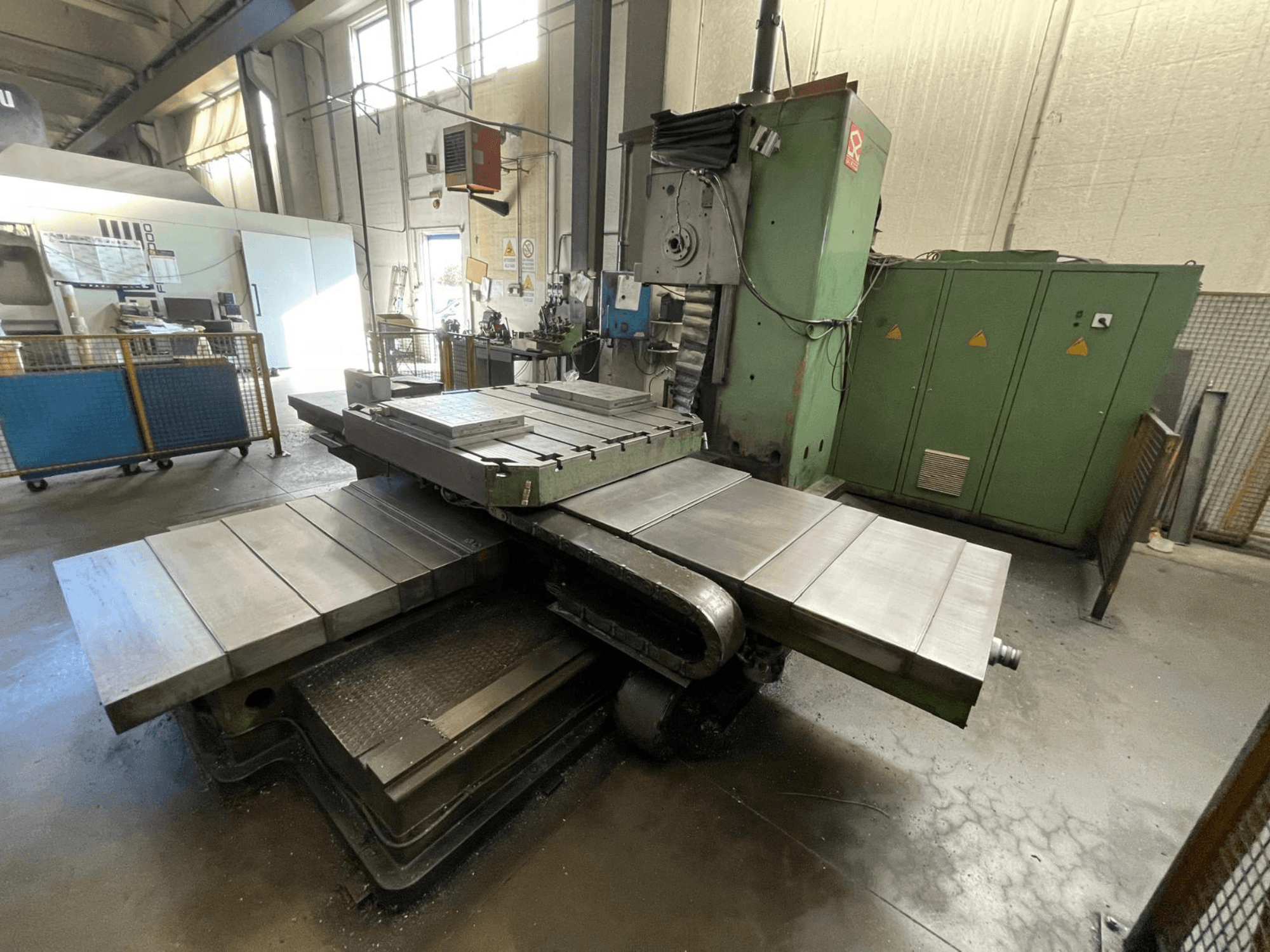 Nagyméretű ipari marógép zöld testtel, oldalnézetben, több sík felülettel és a háttérben tárolószekrényekkel.