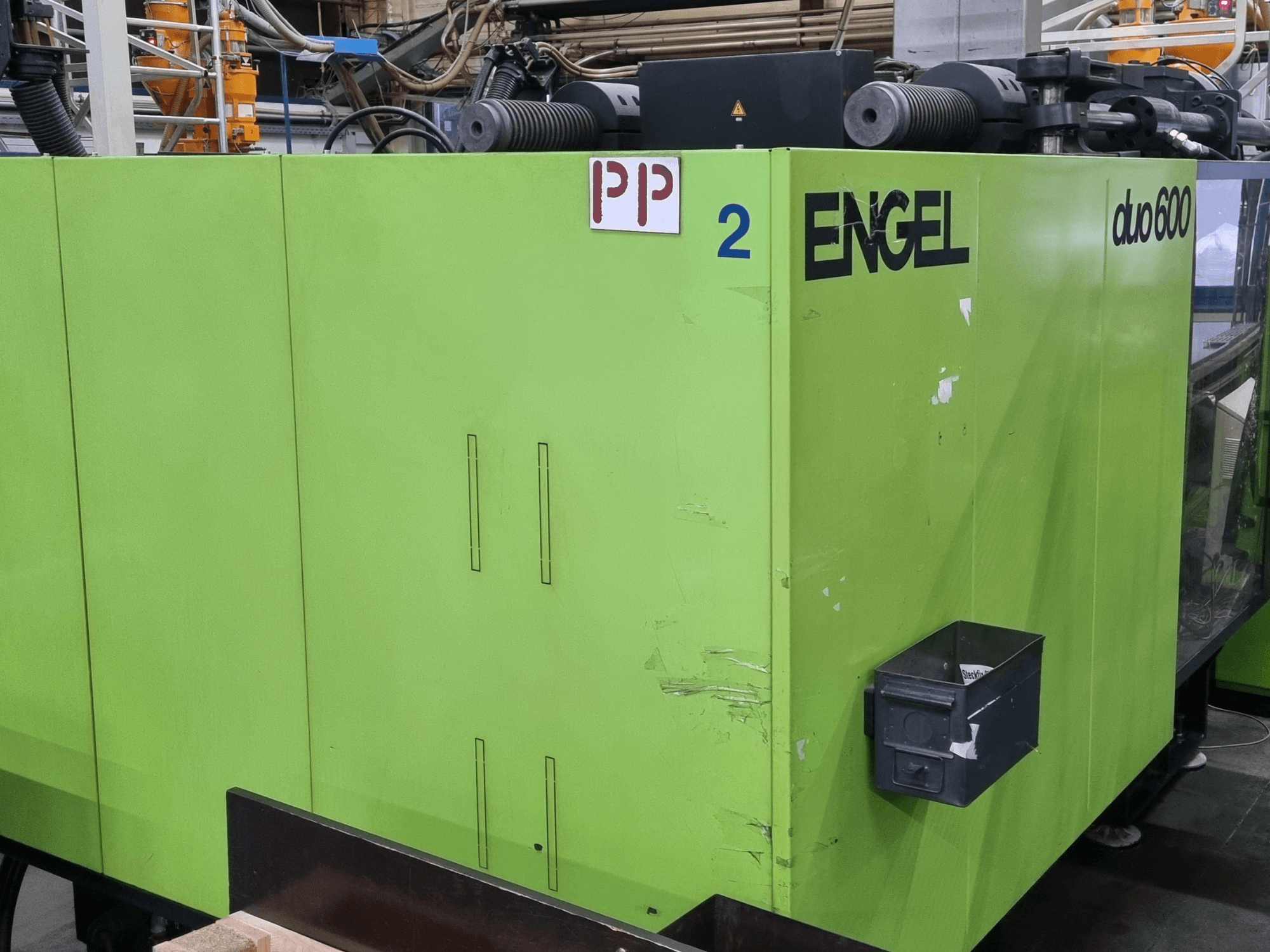 Engel Duo 600 hidraulikus fröccsöntőgép, zöld külső, elölnézet, feliratozott alkatrészekkel és anyagtároló dobozzal.
