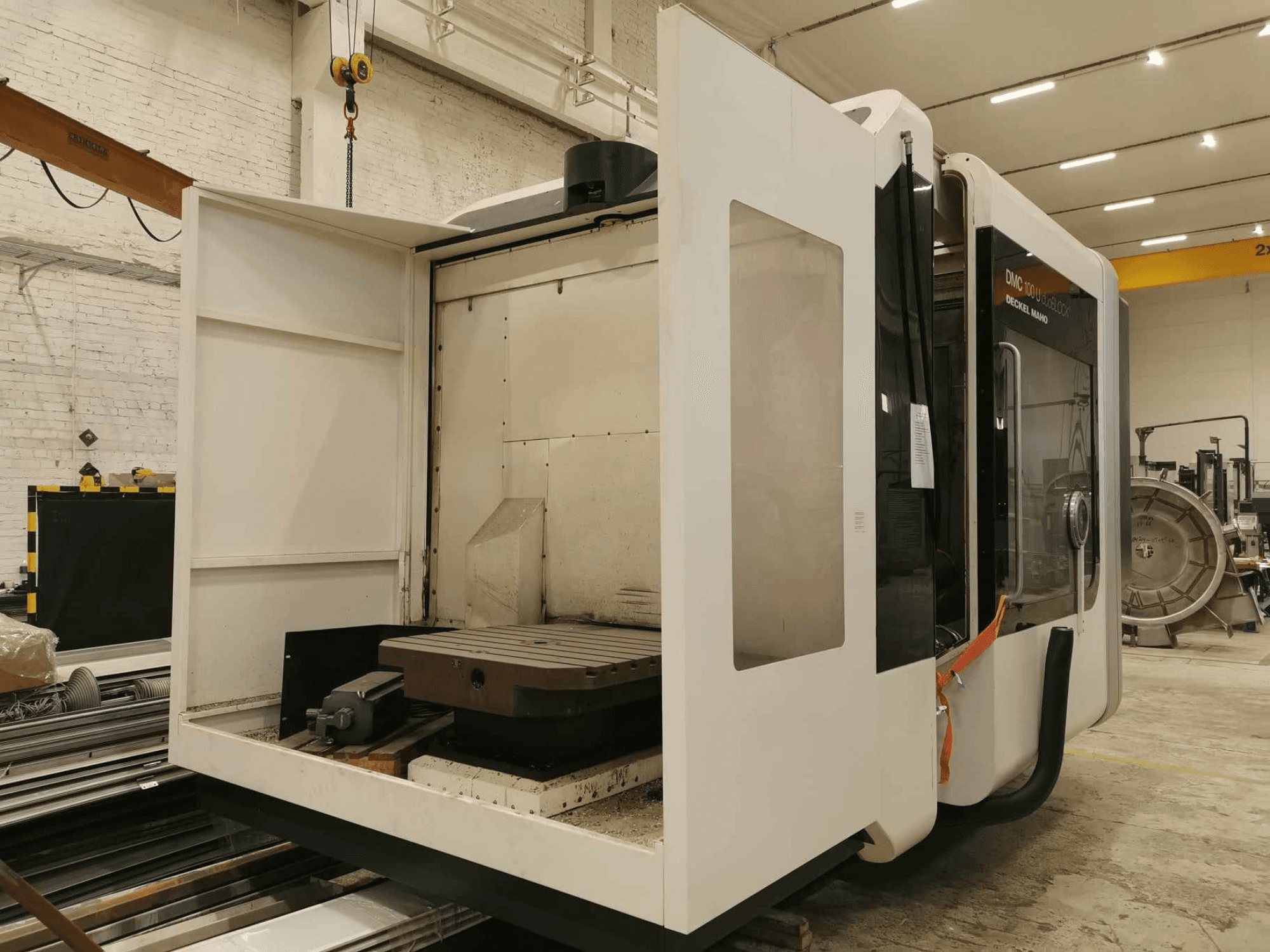 DMC 100U lineáris CNC-gép, oldalnézet nyitott ajtóval, a munkaasztal és a belső alkatrészek láthatóak.