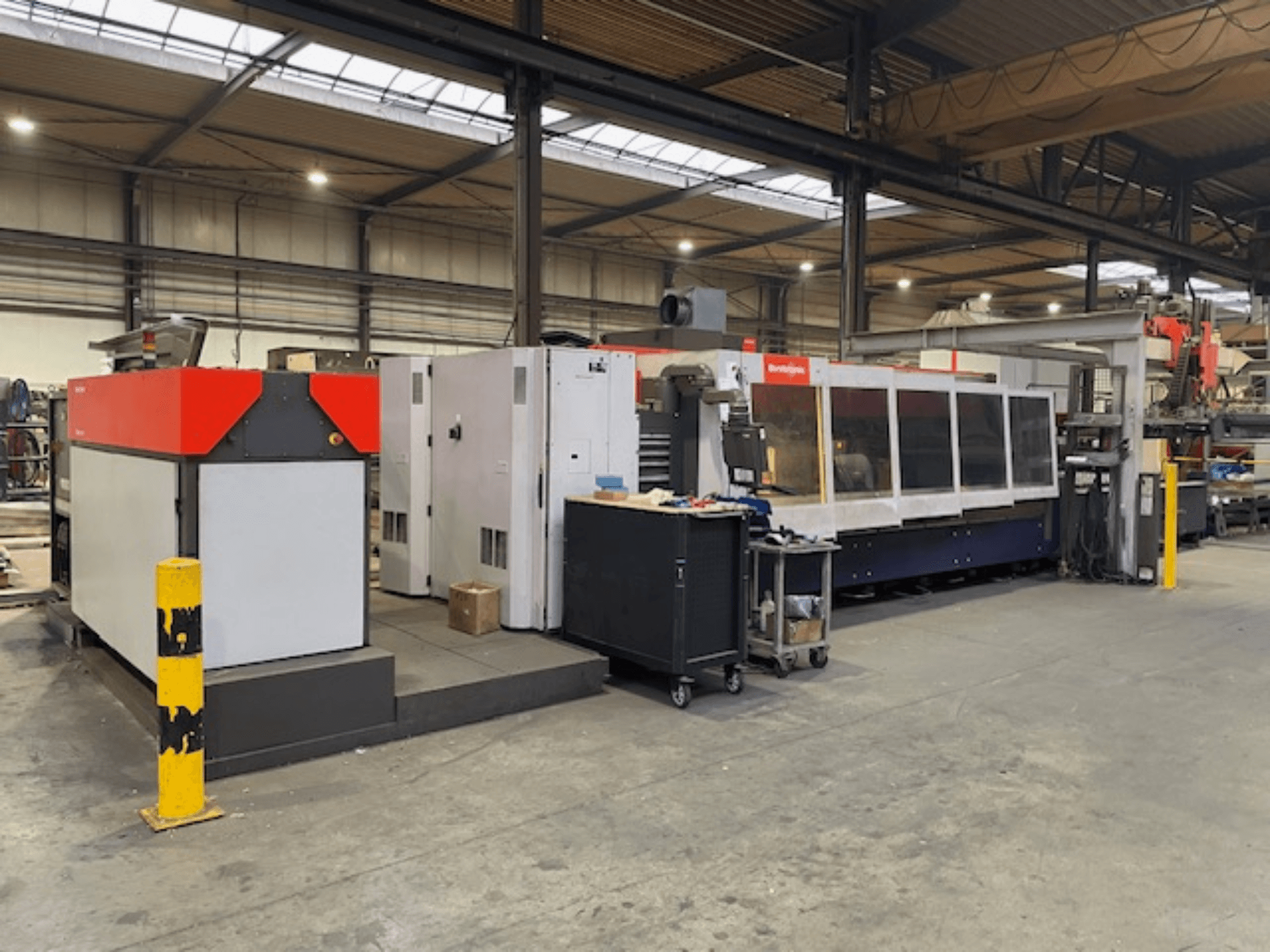 Bystronic BySpeed 3015 CO2 lézervágó gép, oldalnézet egy műhelyben, jellegzetes piros és szürke dizájnelemekkel.