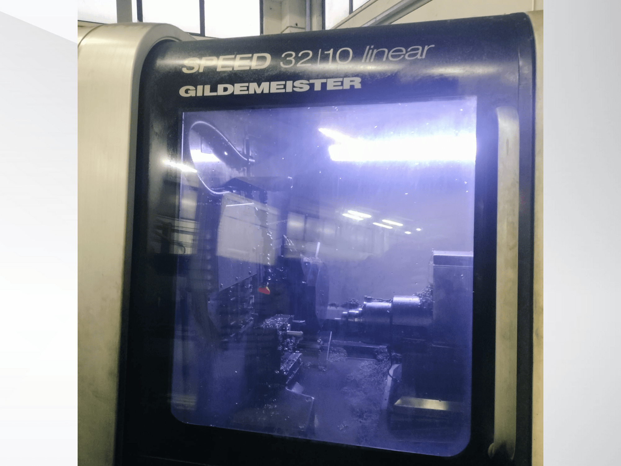 Gildemeister SPEED 3210 lineáris CNC-gép előlnézetben, a belső alkatrészek és a folyékony hűtőfolyadék látható működés közben.