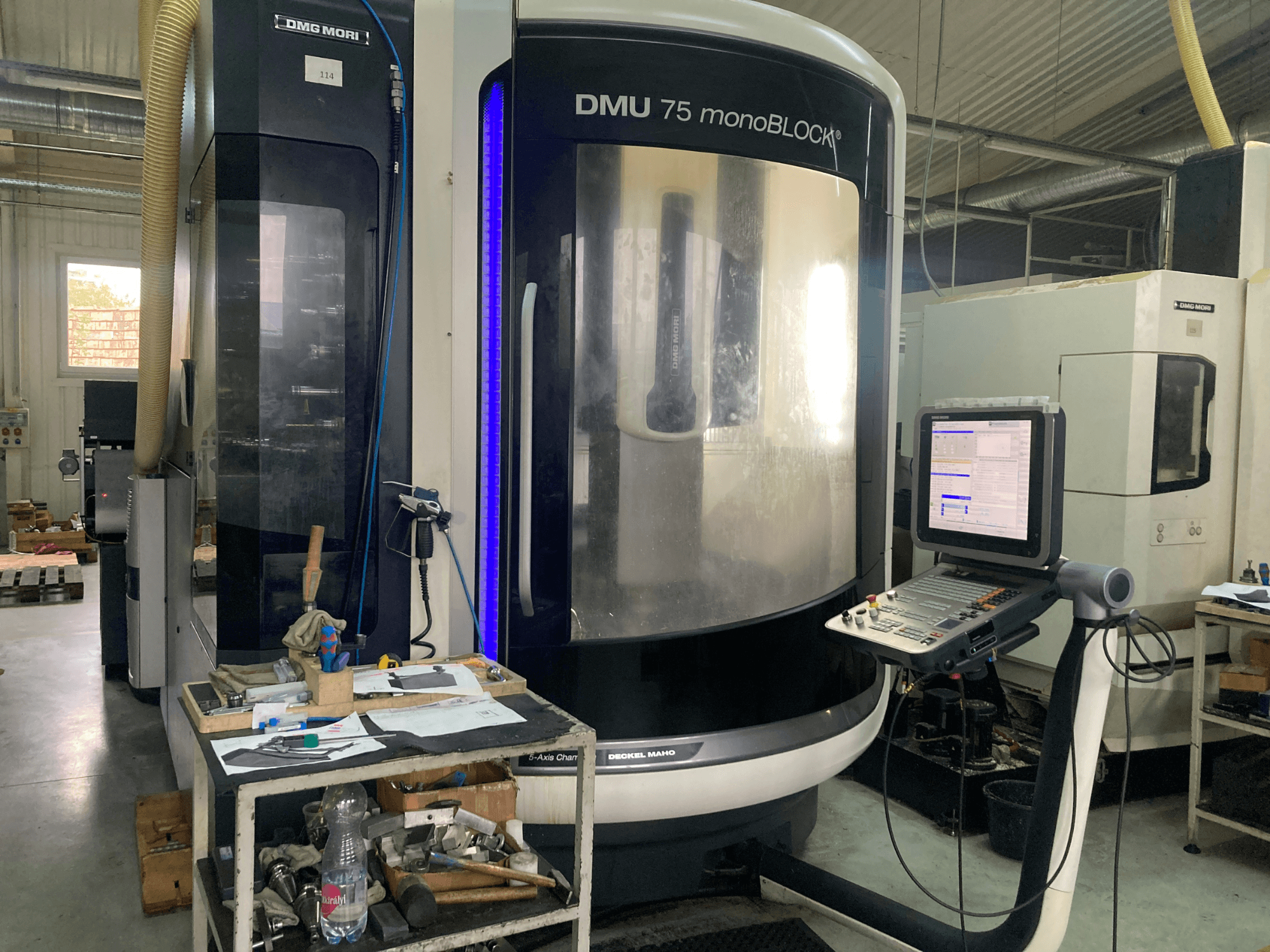 DMG MORI DMU 75 monoBLOCK® CNC gép, előlnézet, a vezérlőpanel, a szerszámok és az anyagokkal ellátott munkaterület.