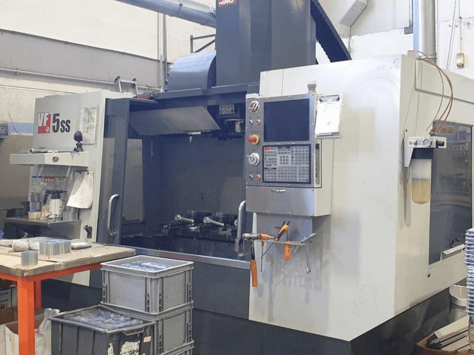 HAAS VF-5SS függőleges megmunkálóközpont elölnézetben, a vezérlőpanel, a munkaterület és a tárolórekeszek.