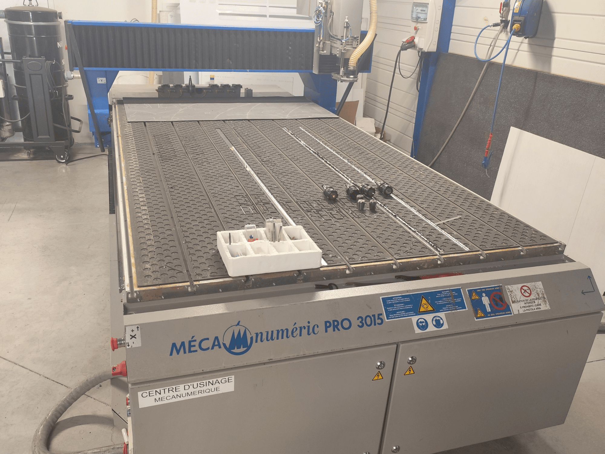 A MECANUMERIC Pro 3015 CNC-marógép elölnézete, amelyen jól látható a vágóasztal, a vezérlőpanel és az asztalon elhelyezett kiegészítők.