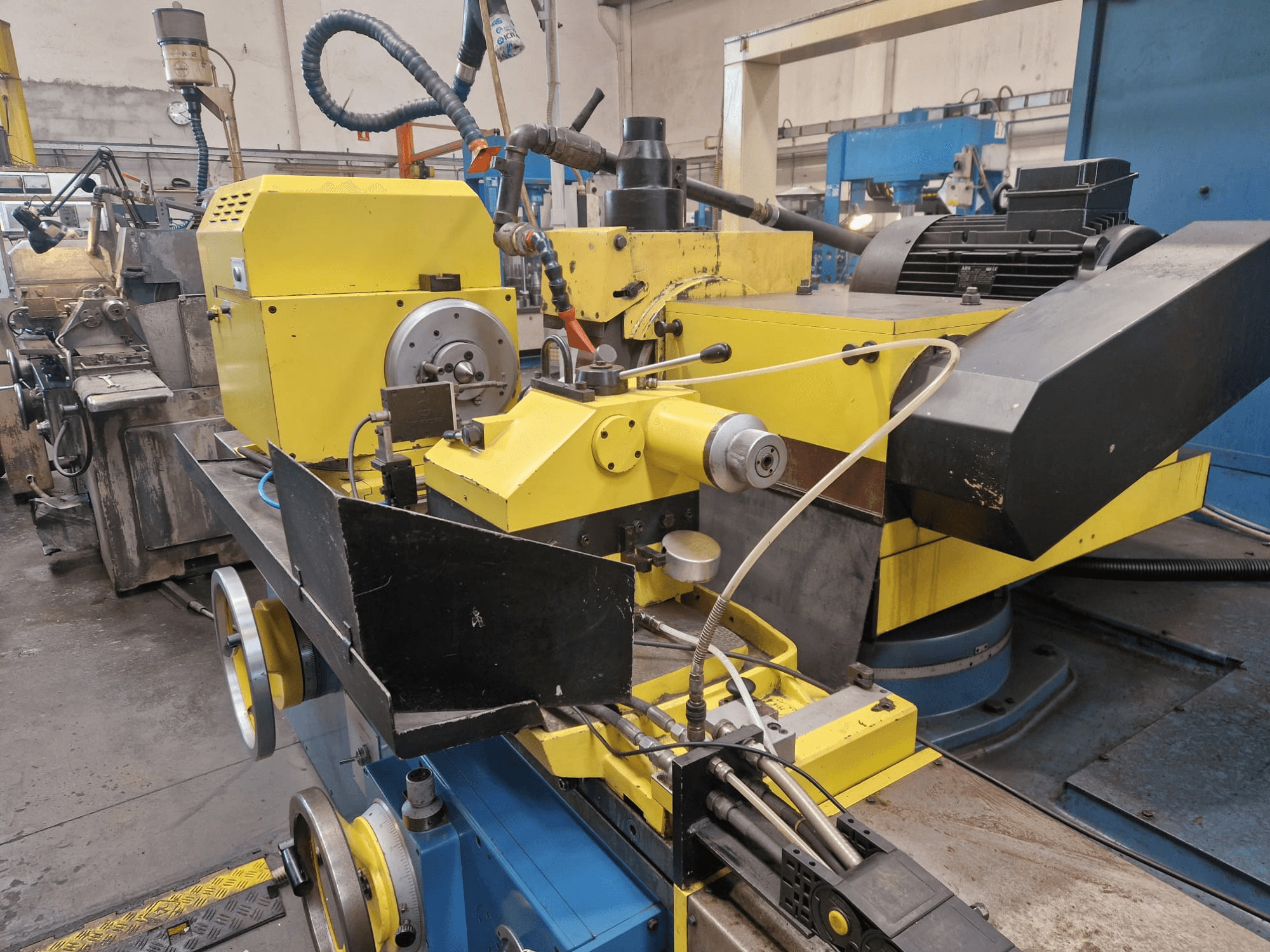 Sárga ipari gép, fekete részleggel, tárcsával és tömlőkkel, elölről, enyhe szögből nézve.