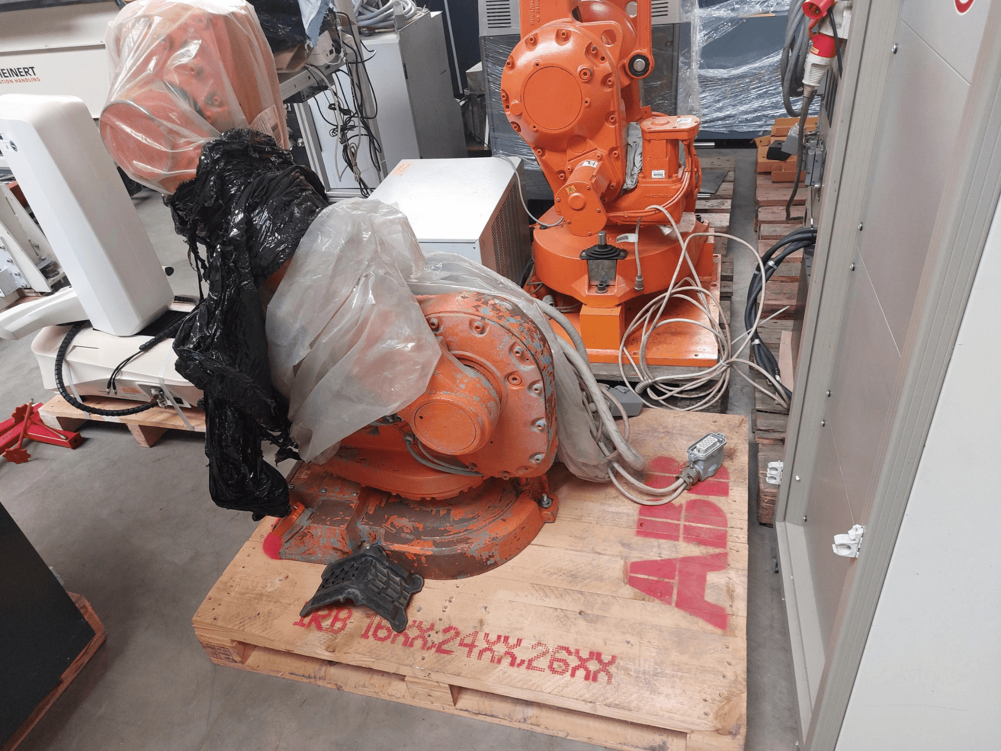 ABB IRB 1600 M2004 robotkar, részben műanyaggal borítva, szemből nézve, a közelben kábelek és további gépek.