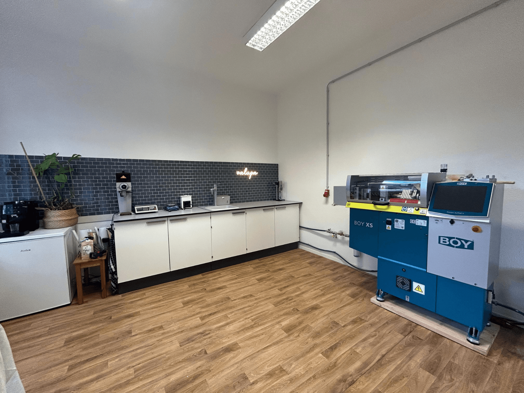 Hidraulikus fröccsöntőgép BOY XS 161, elölnézetben, modern konyhai környezetben, készülékekkel és fa padlóburkolattal.