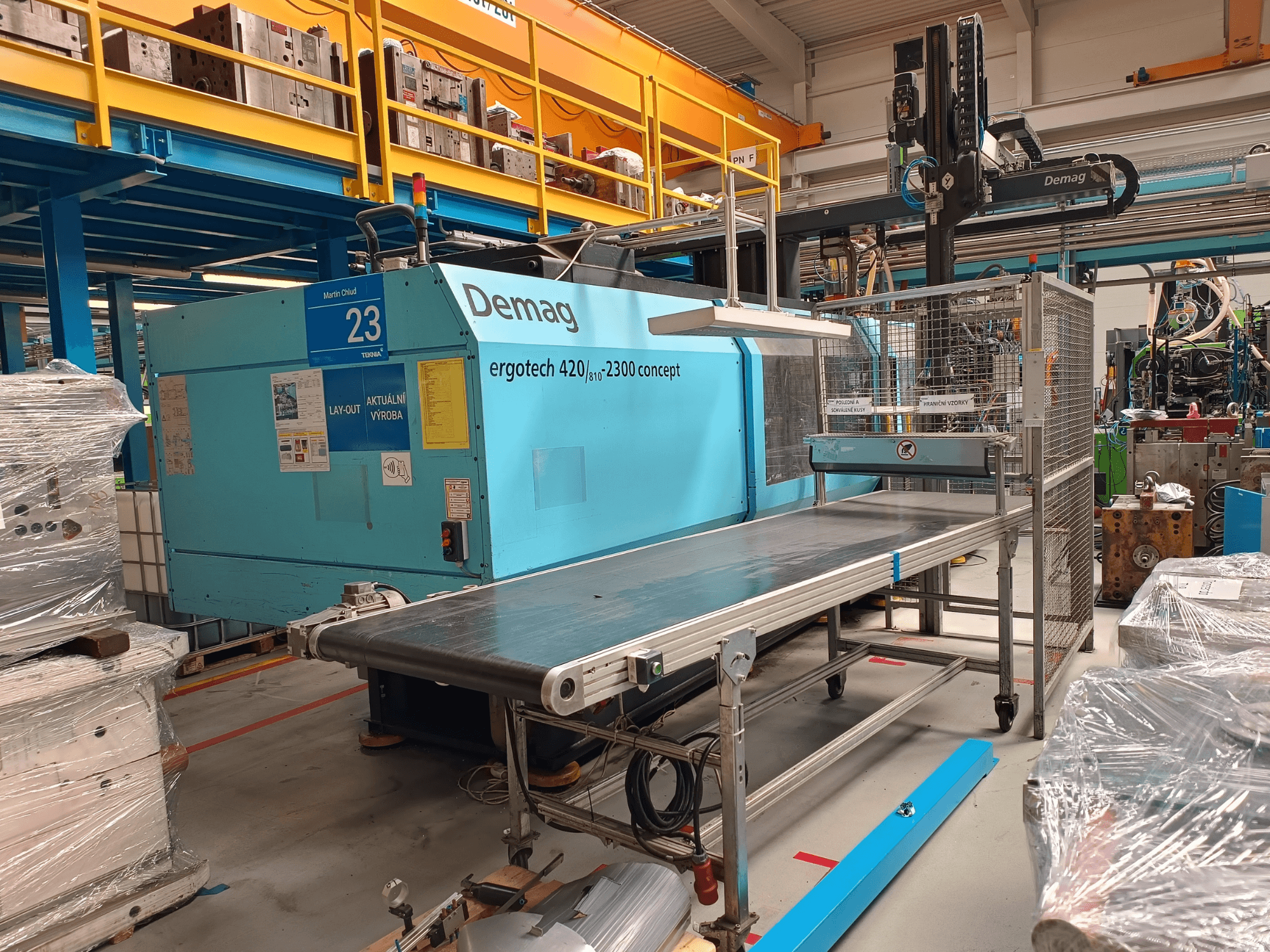 Demag ergotech 420/810 - 2300 hidraulikus fröccsöntőgép oldalnézetben, szállítószalaggal és biztonsági burkolattal.