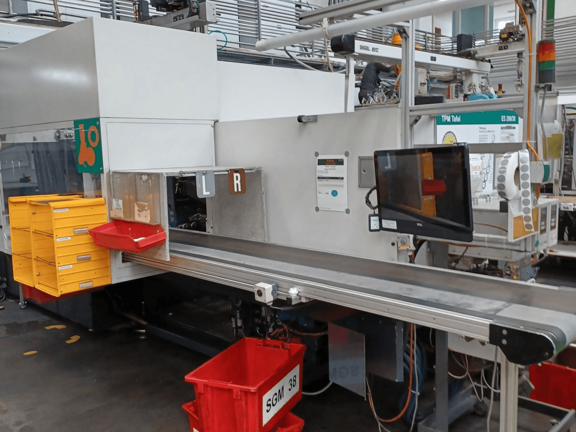 Ipari válogatógép sárga és piros tárolókkal, oldalnézetben, vezérlő monitorral és felcímkézett rekeszekkel a válogatáshoz.
