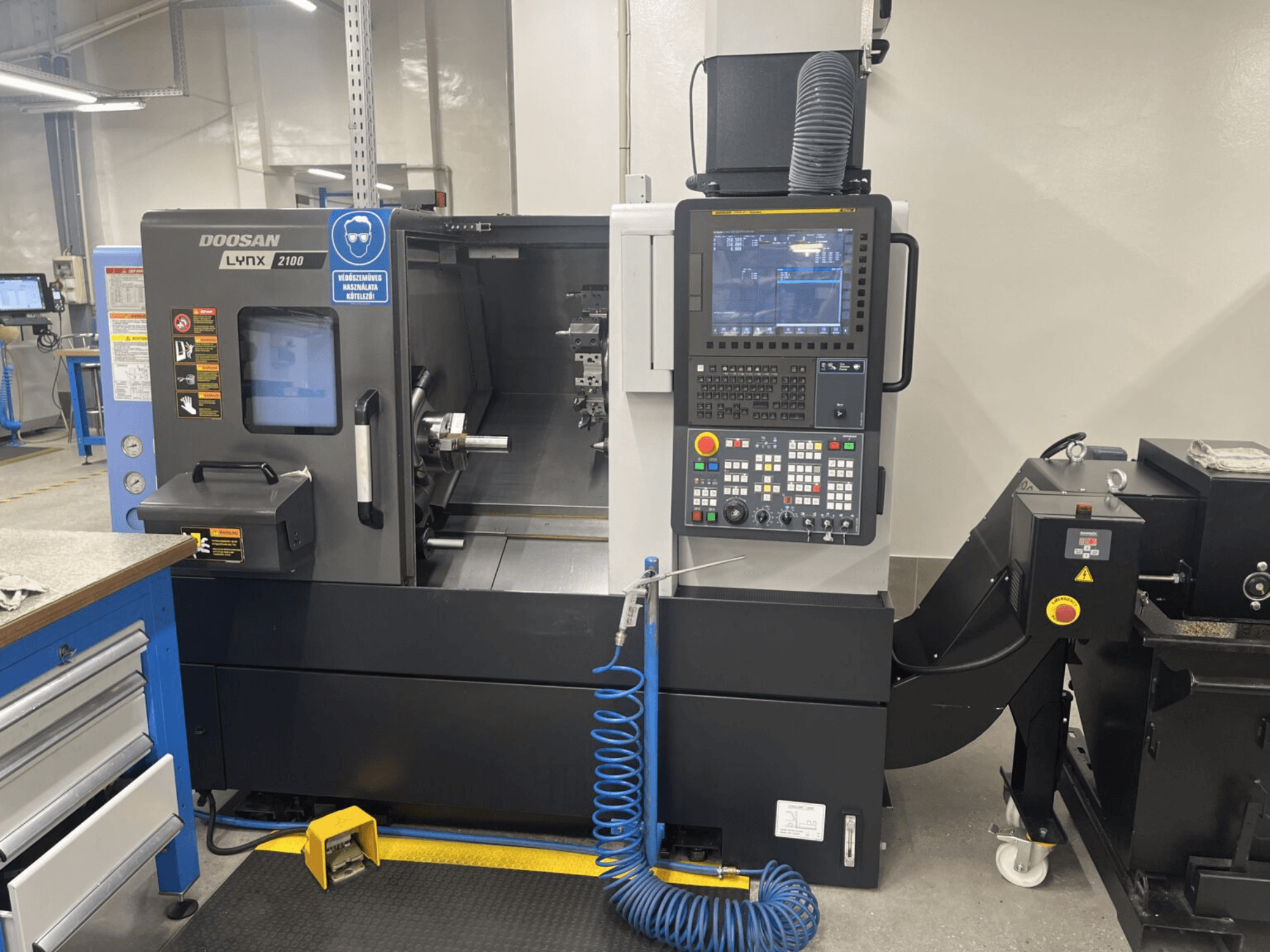 Egy DOOSAN Lynx 2100A vízszintes esztergagép elülső nézete, amely a vezérlőpanelt és az orsó területét mutatja a figyelemre méltó biztonsági funkciókkal.