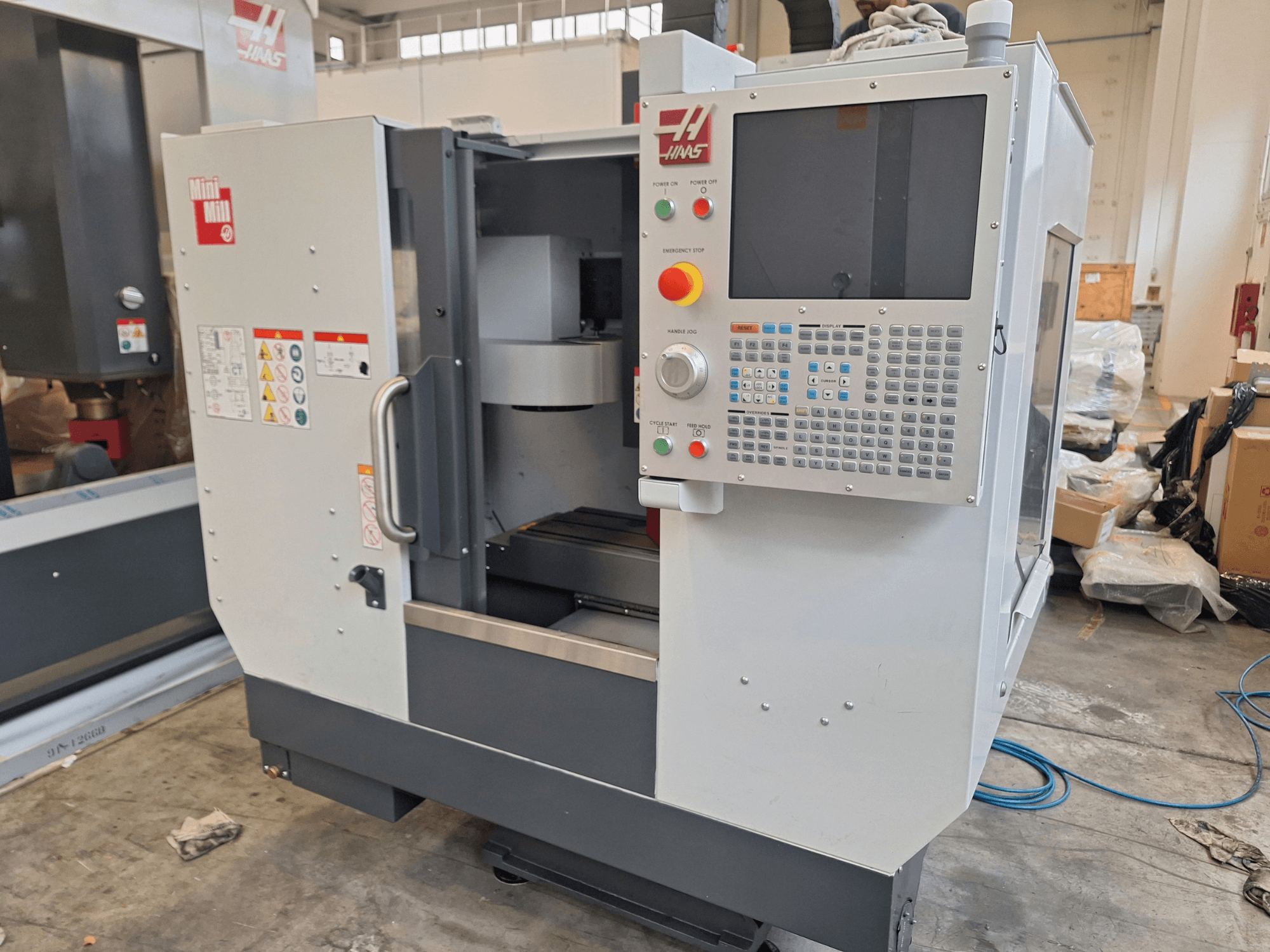 A HAAS Mini Mill függőleges megmunkáló központ elölnézete, gombokkal ellátott vezérlőpanellel és kijelzővel.