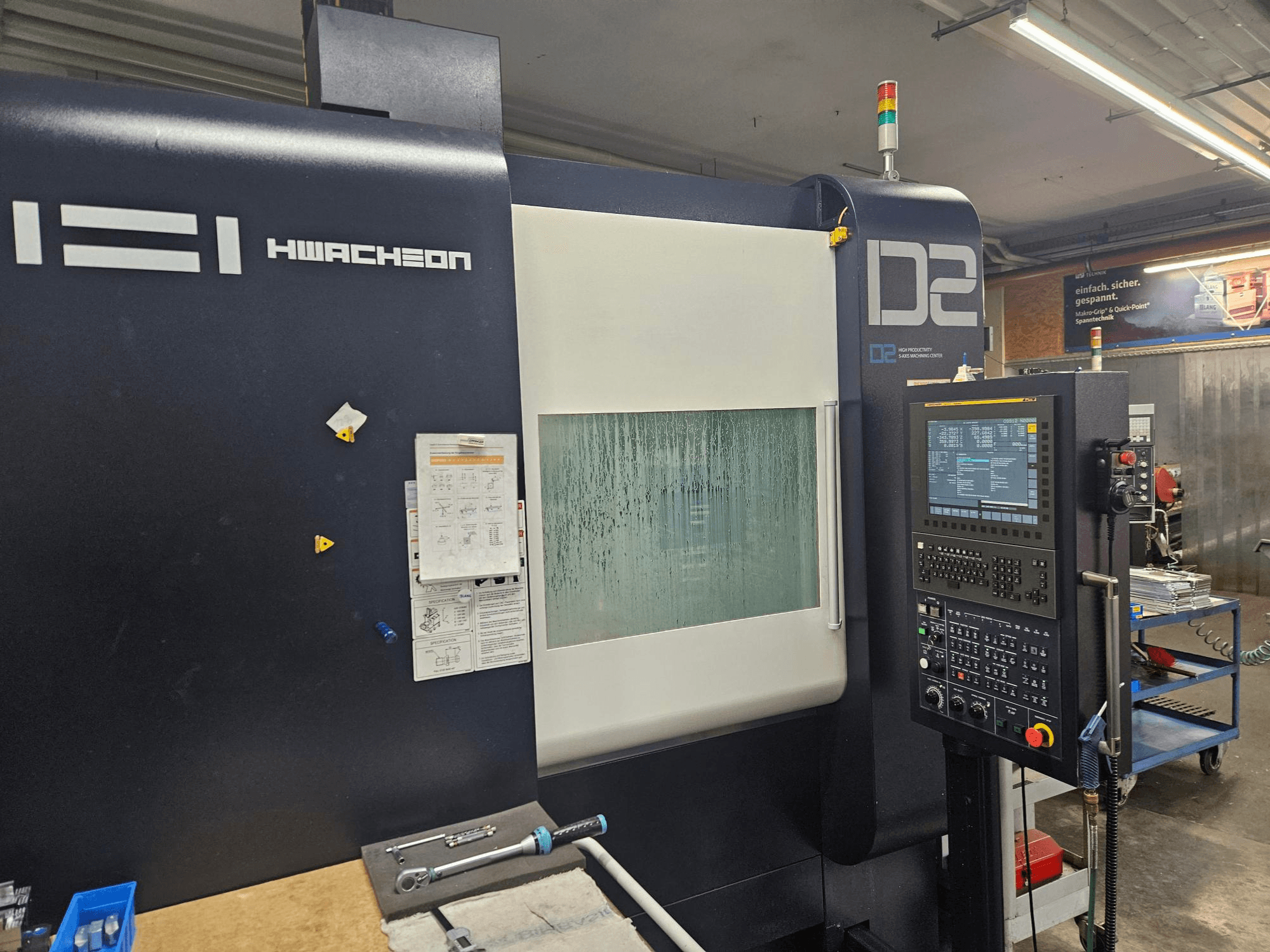 HWACHEON D2-5AX 12k függőleges megmunkáló központ, elölnézet a vezérlőpanellel és a párásodott ablakkal.