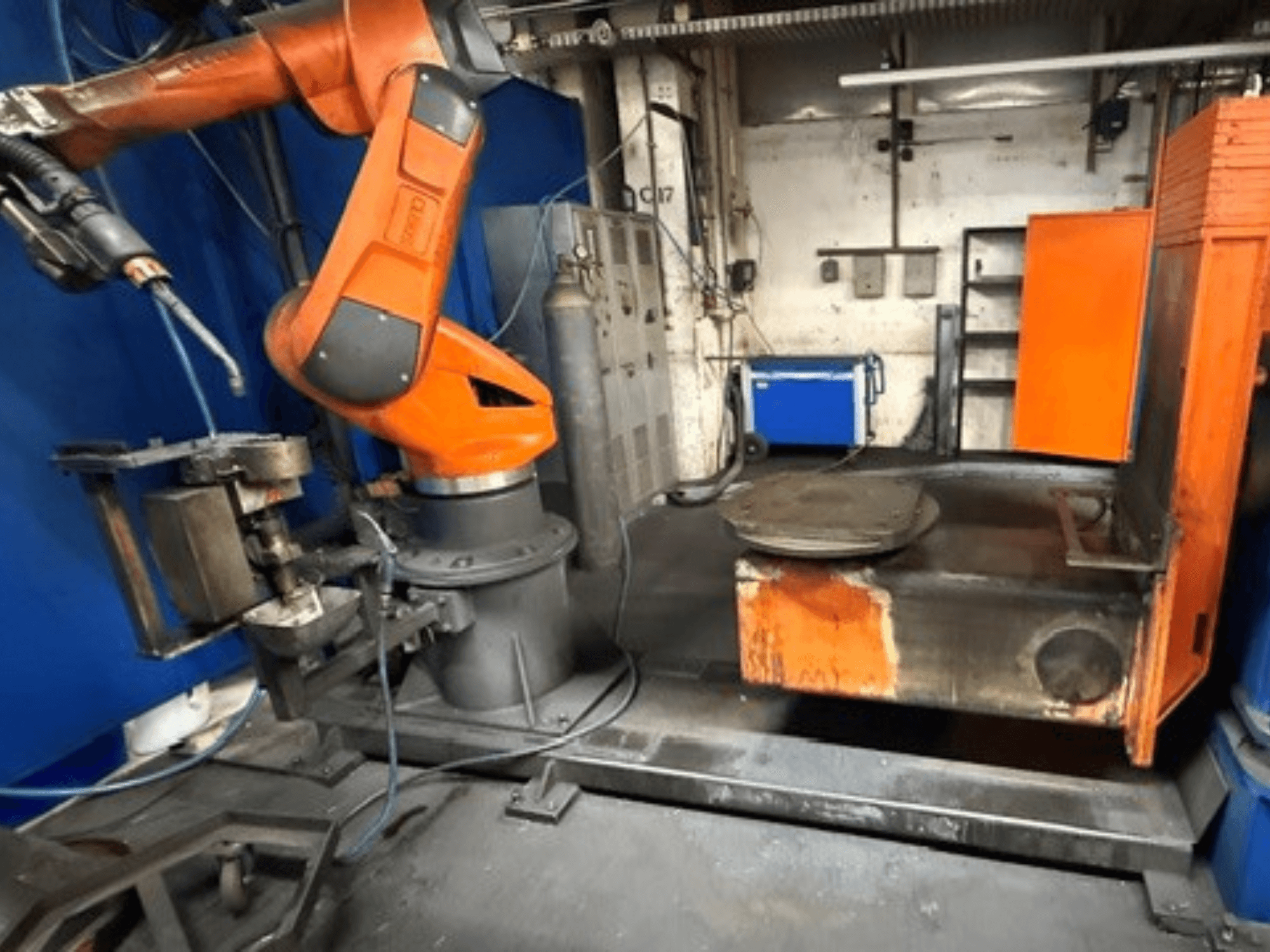 A CLOOS C50 hegesztőrobot elölnézetben, narancssárga robotkarral és fém munkapaddal.