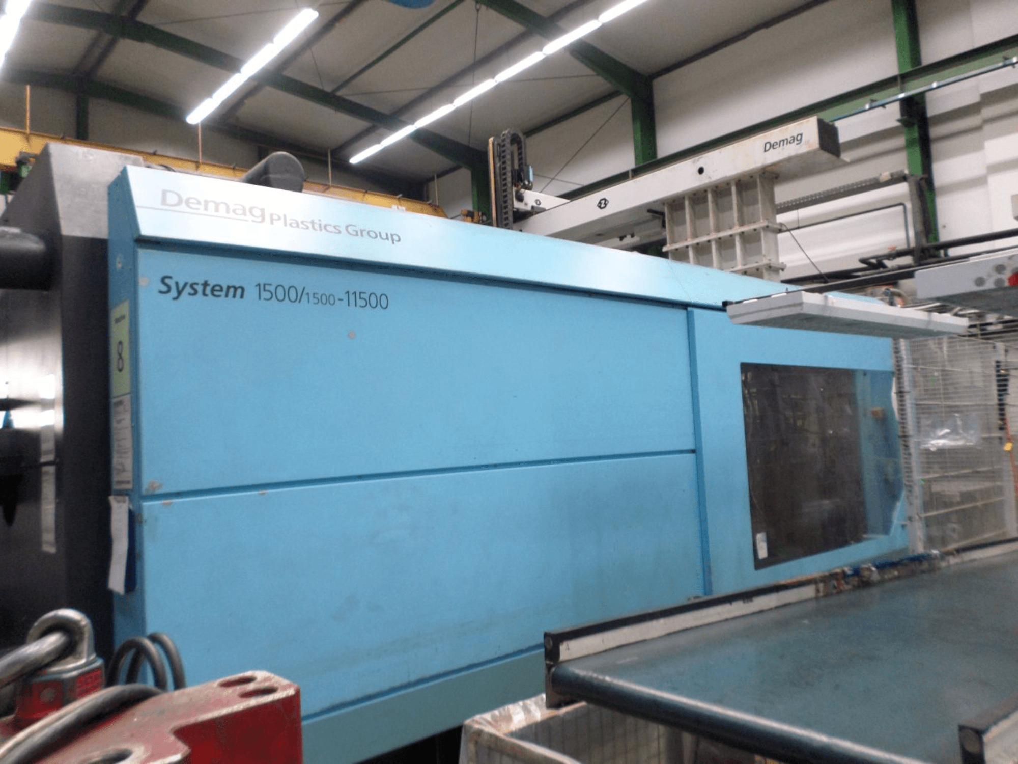 Kék színű Demag D 650 hidraulikus fröccsöntőgép, oldalnézet, amelyen látható a „System 1500/1500-11500” felirat és a kezelőfelület.