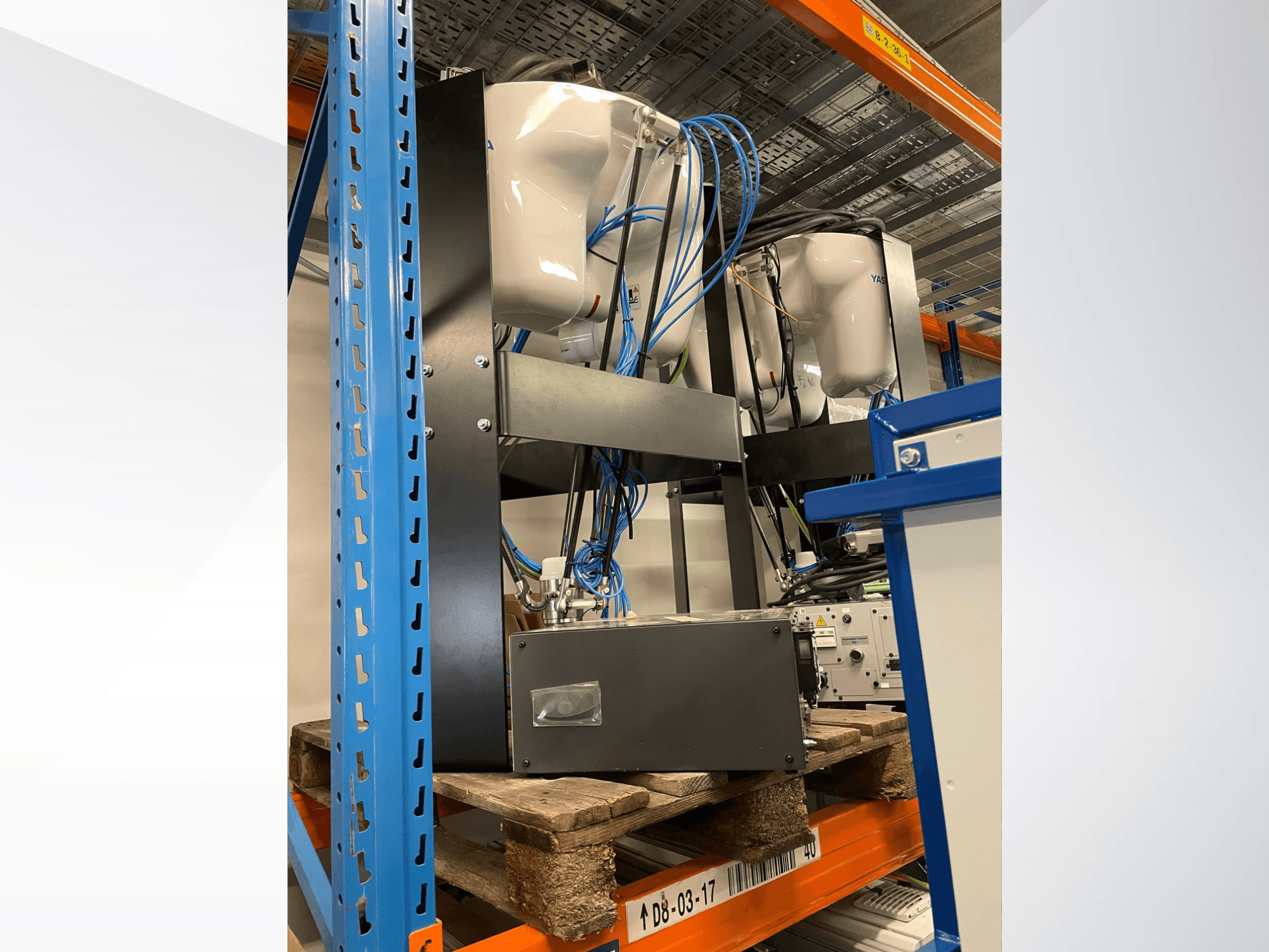 Yaskawa Motoman MPP3H robotkar oldalnézetben, a kábelekkel és alkatrészekkel együtt, egy tárolópolcon.