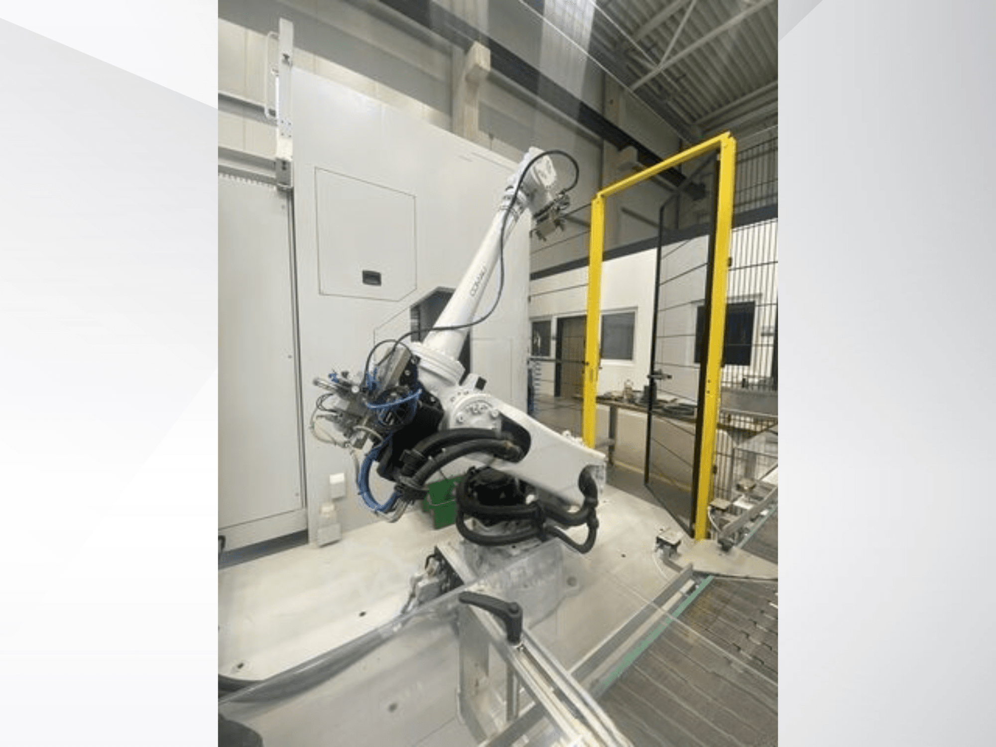 COMAU Smart NJ 40-2.5 robotkar oldalnézetben, kábelekkel és sárga biztonsági kapuval, gyári környezetben.