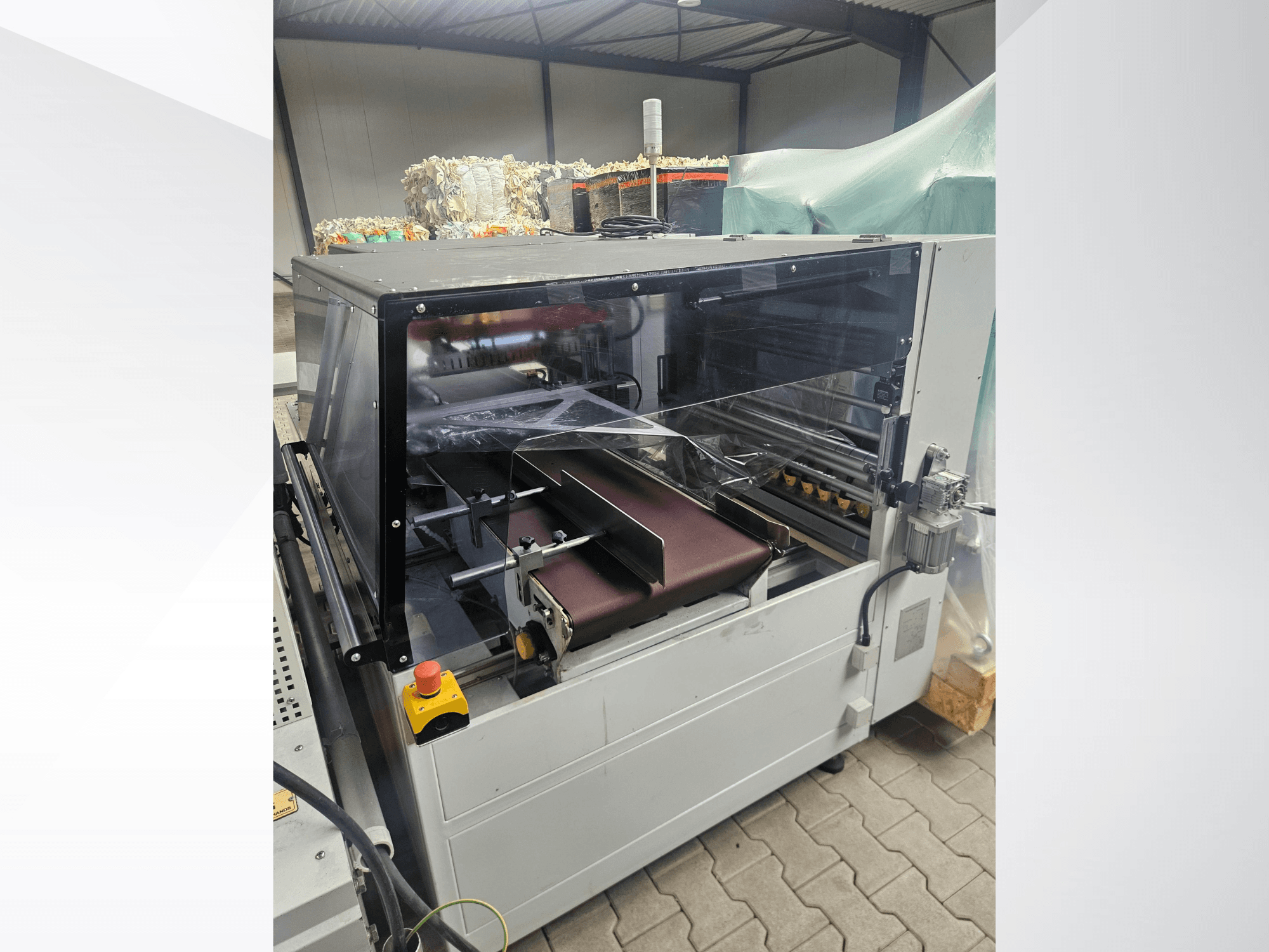AMTEC Speed Shrink 40 PRO gép, elölnézet, amelyen látható a műanyag-feldolgozó mechanizmus átlátszó biztonsági burkolattal és szállítószalaggal.