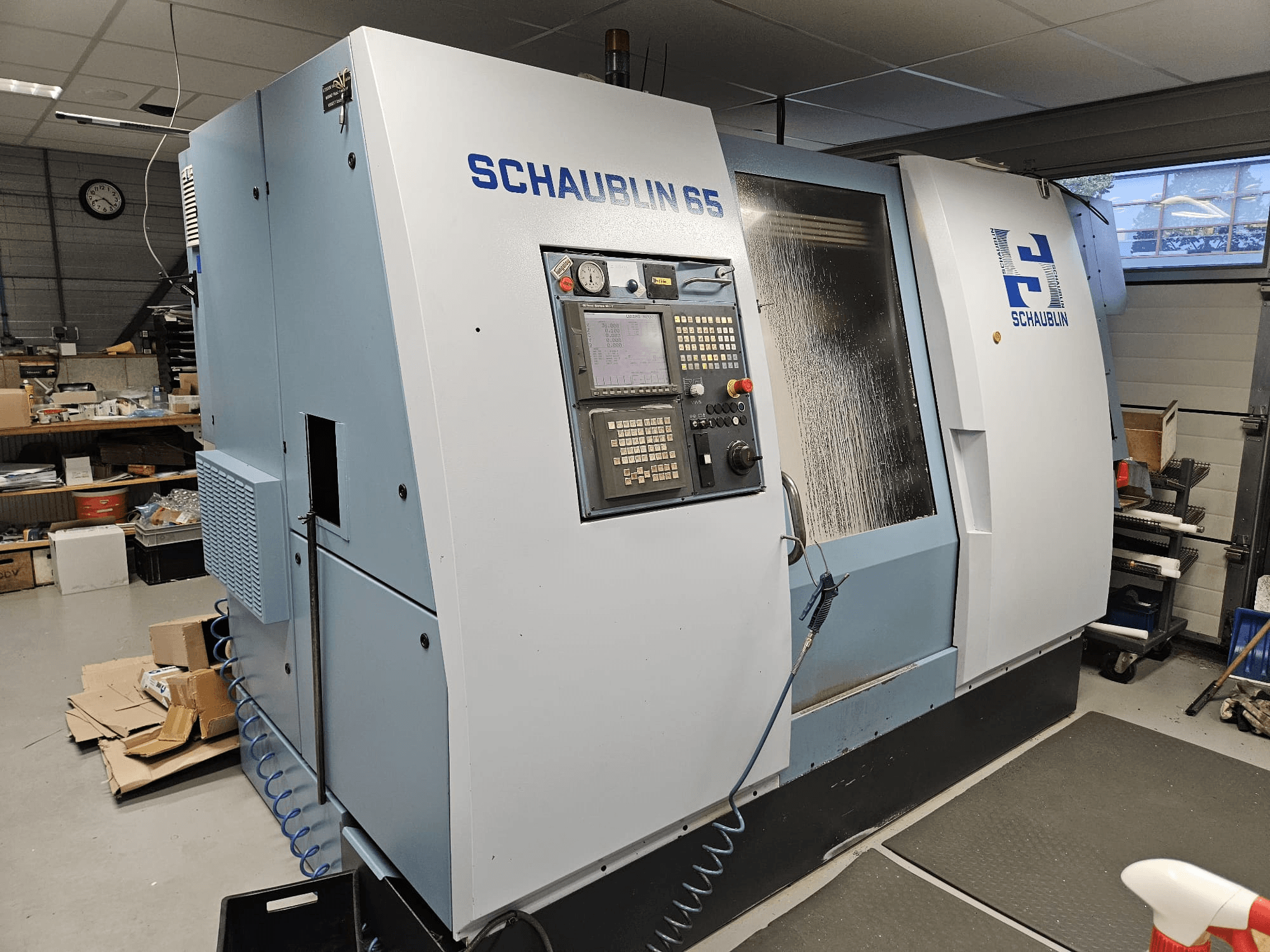 SCHAUBLIN 65 CNC-gép, oldalnézet, vezérlőpanel, kék és szürke burkolat, látható hűtőfolyadék-rendszer.