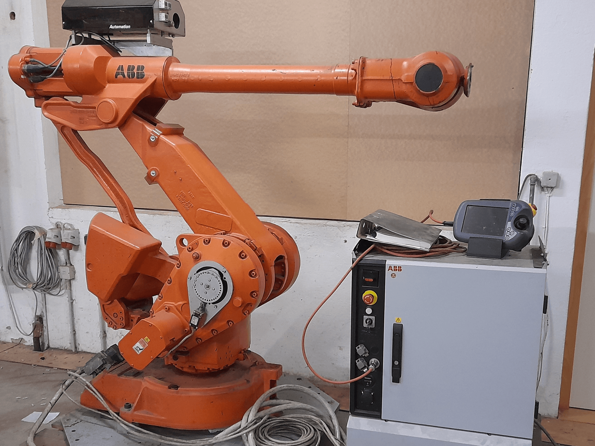 Narancssárga ABB robotkar vezérlőpanellel, elölnézetben, kábelek és automatizálási berendezések bemutatásával.